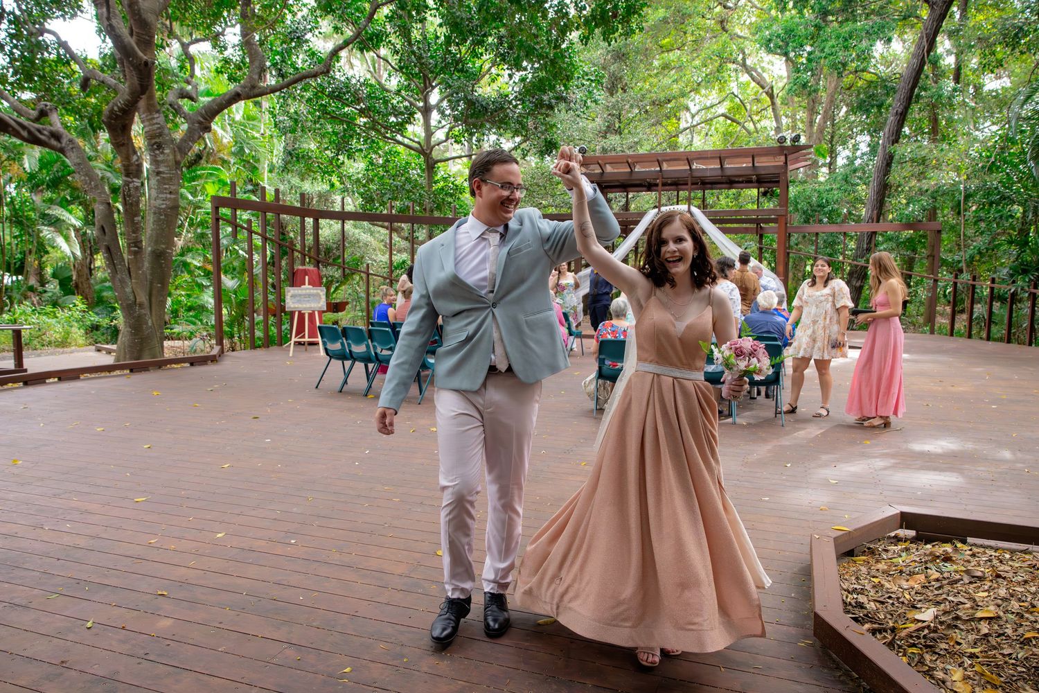 Couple celebrating joyfully on wooden deck surrounded by trees.