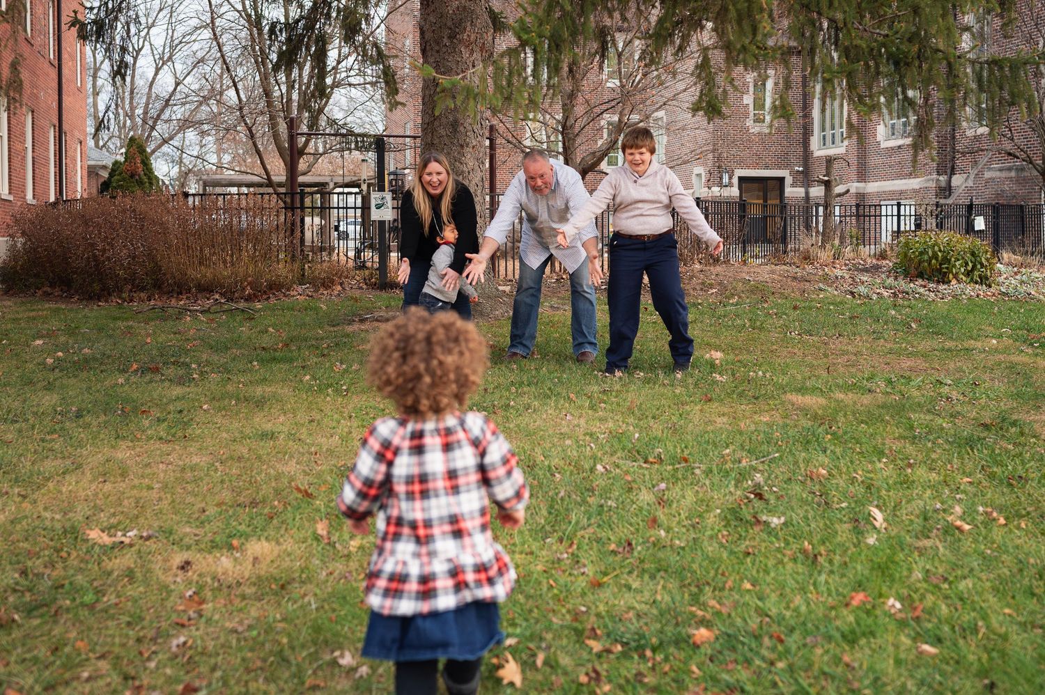 Excited family with arms open as curly-haired toddler runs to them during a winter mini session in downtown Columbus
