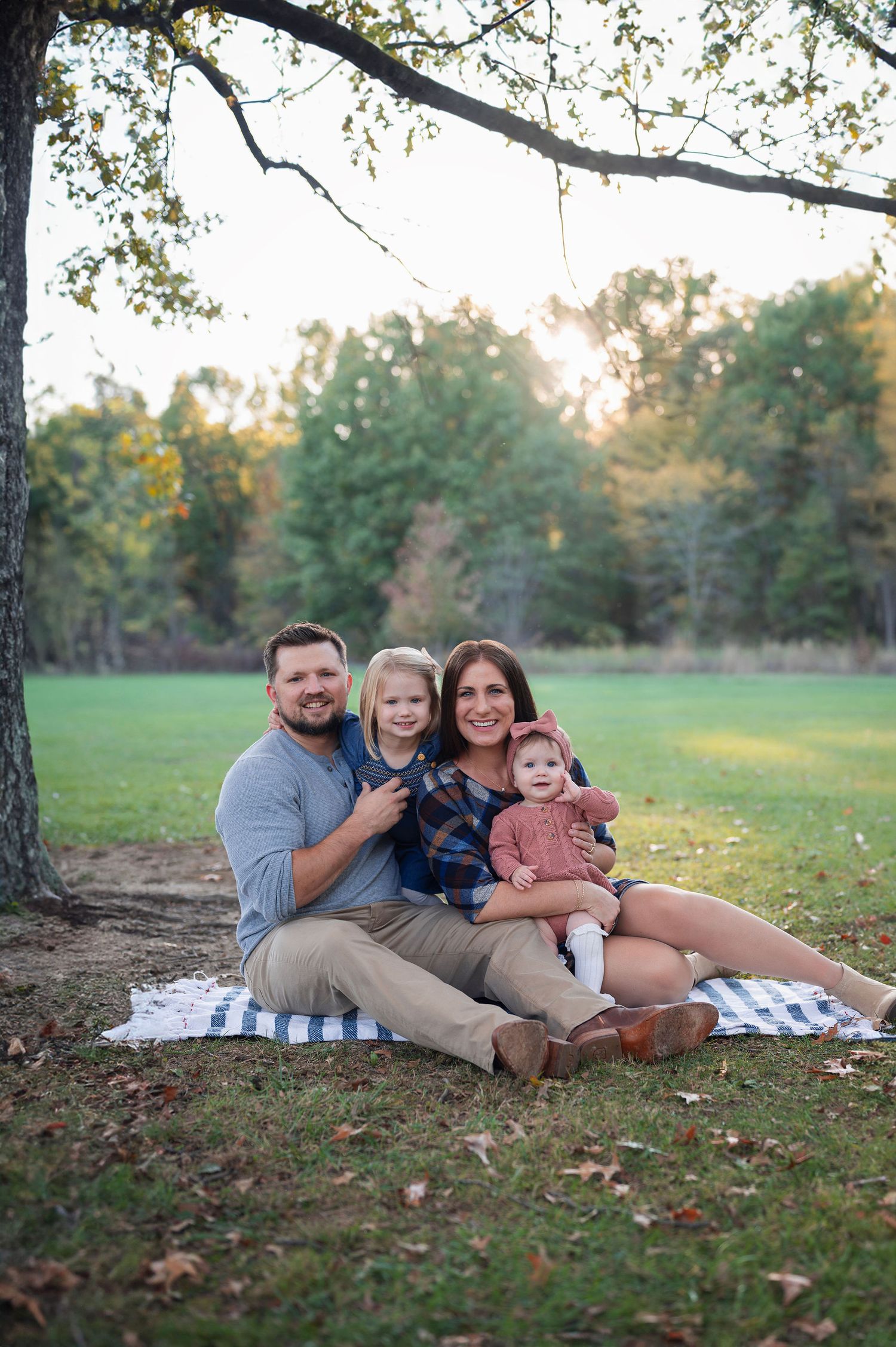 Sharon Woods family session with parents and two young daughters sitting on a blanket under fall trees at golden hour