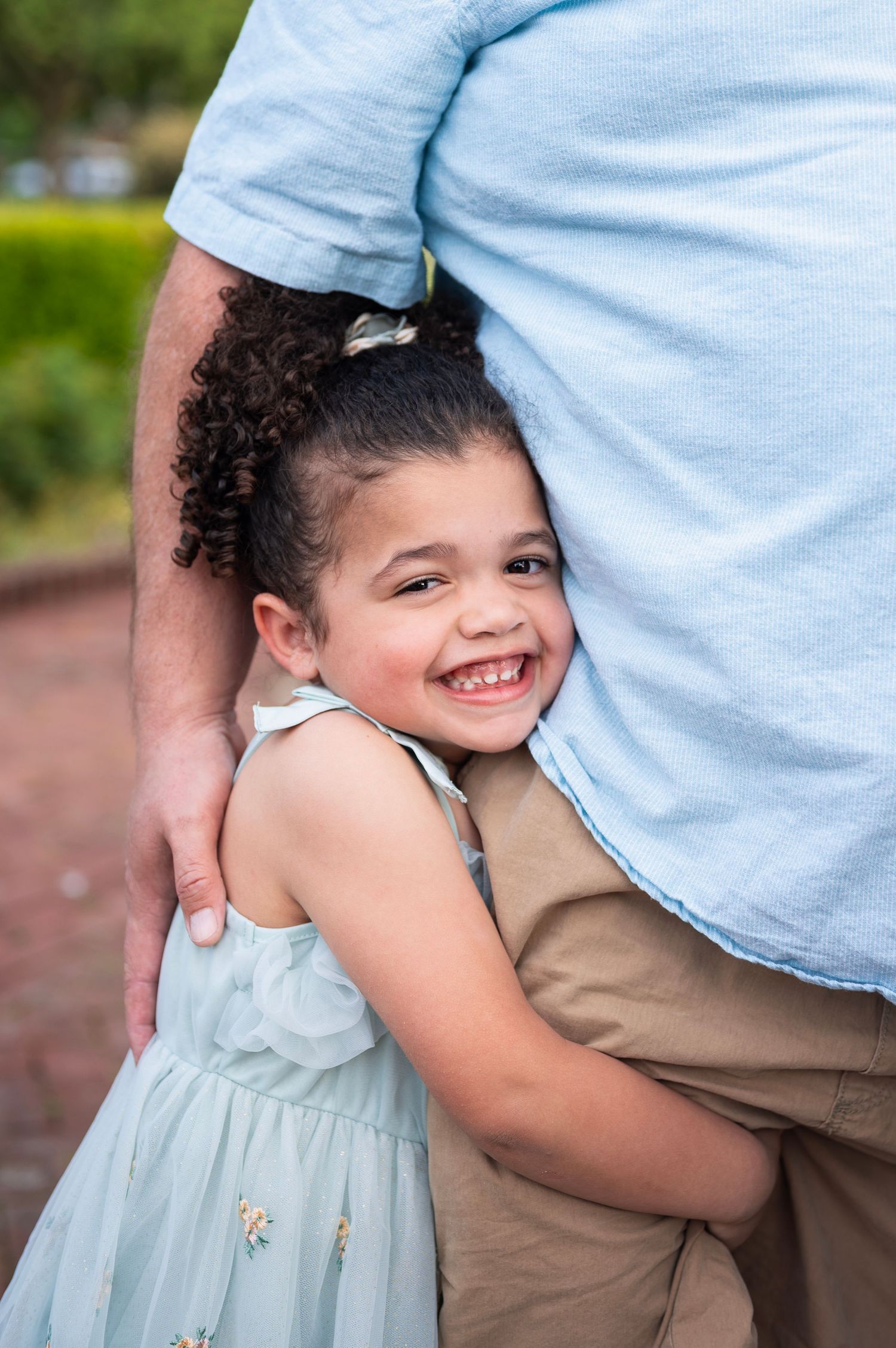 Close-up of smiling child in a blue dress hugging her dad during a warm and playful photo session
