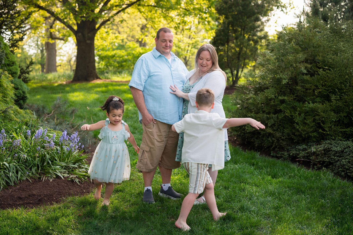 Young siblings twirl around barefoot during a spring garden session with their smiling parents.