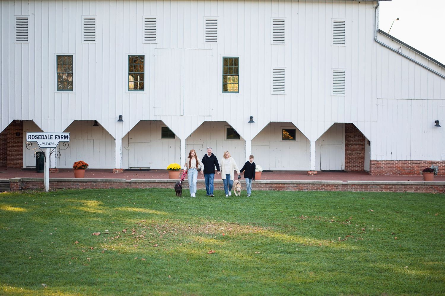 A family of five walks hand in hand with two dogs in front of the white historic Everal Barn in Westerville.