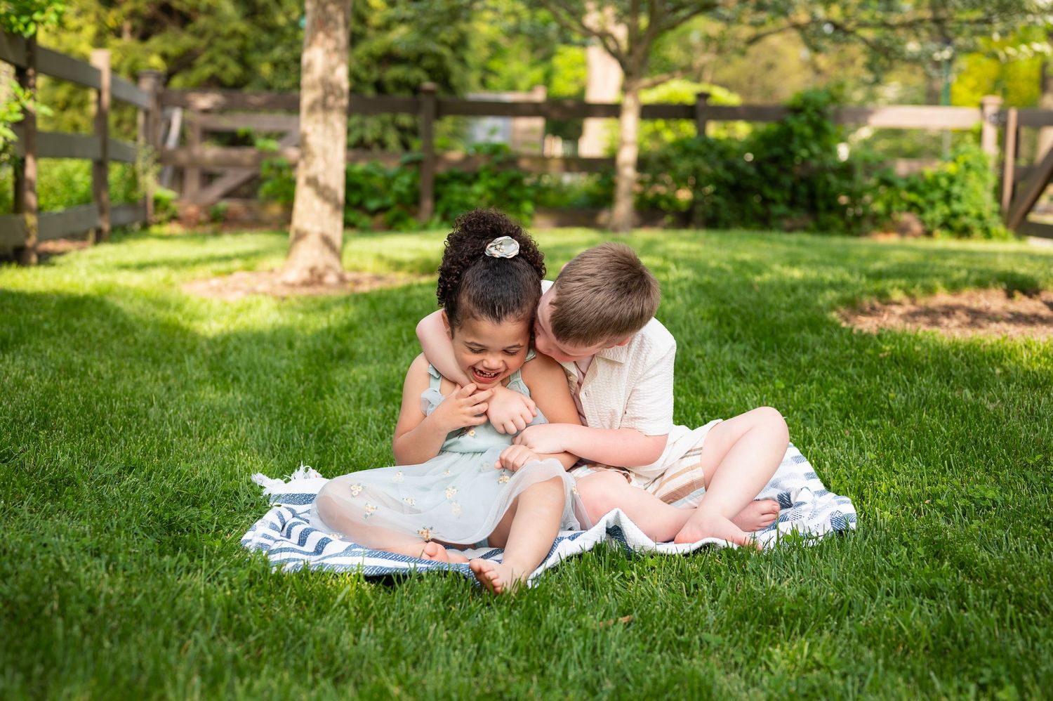 Siblings giggling during a spring family session at Franklin Park, sitting barefoot on a blanket