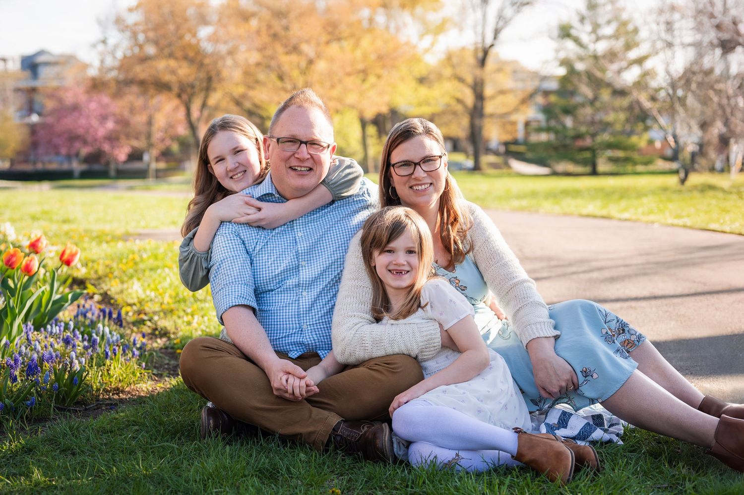 Family of four cuddled together in a spring park, surrounded by tulips and sunshine — Westerville family photographer