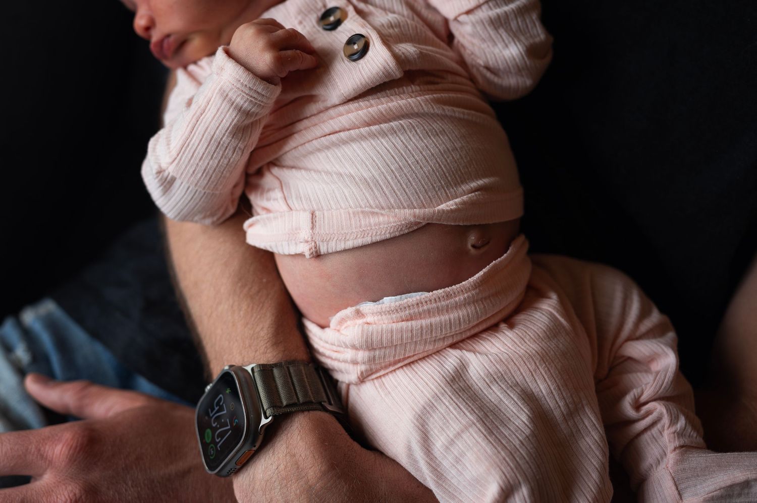 Close-up of newborn’s tummy and umbilical stump as she rests on dad’s lap in soft, natural light.