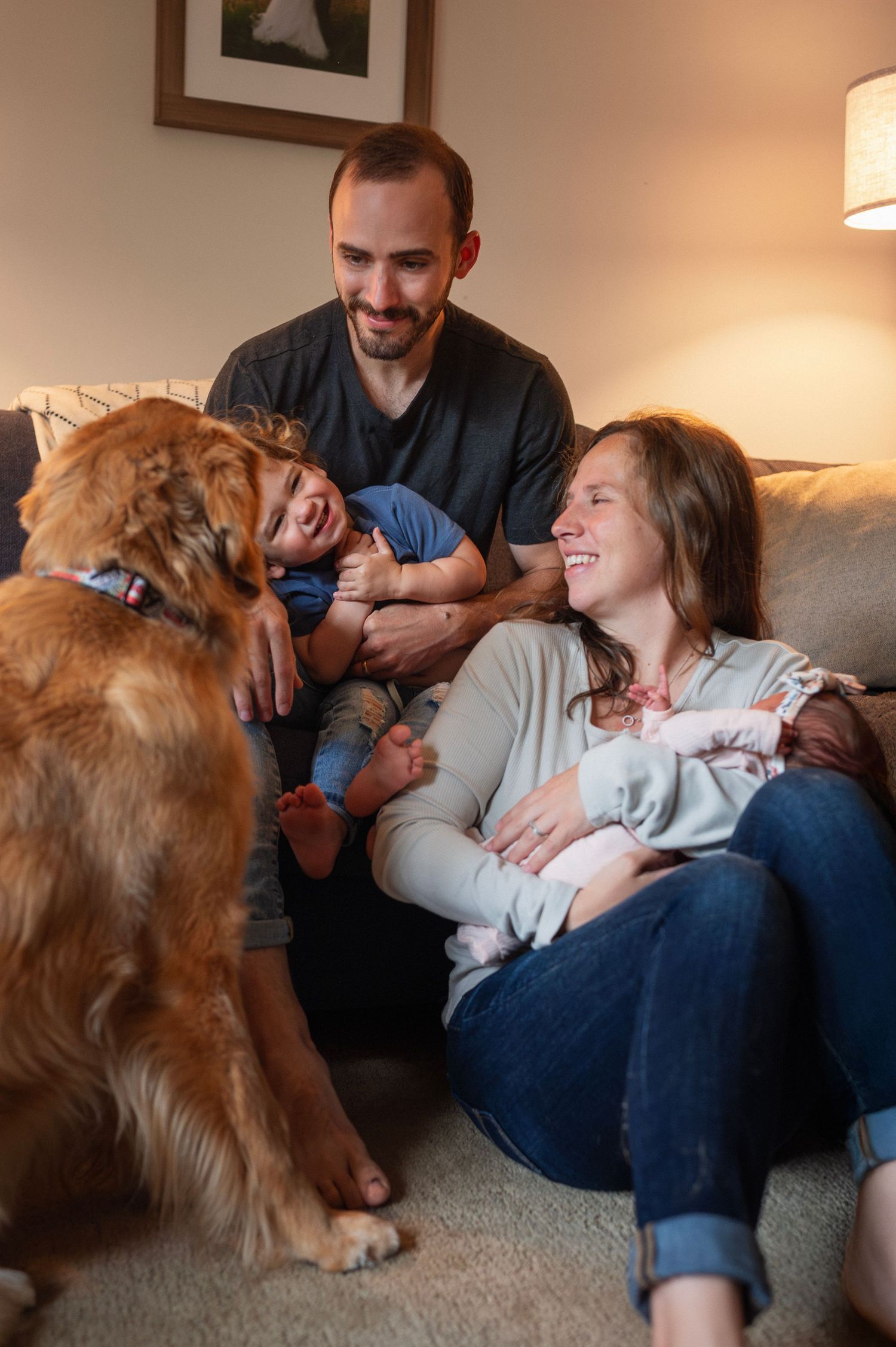 Family cuddles with newborn and toddler during cozy indoor session in Columbus with their golden retriever.
