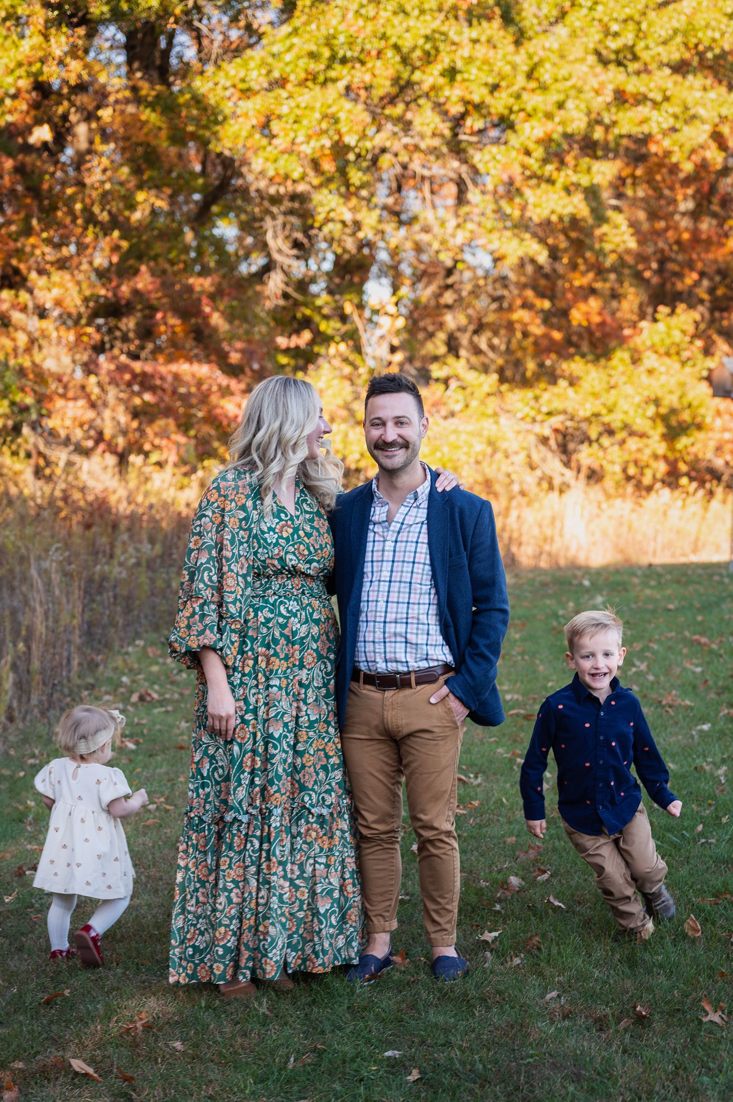 Parents share a sweet moment while their kids play nearby in a glowing fall field.