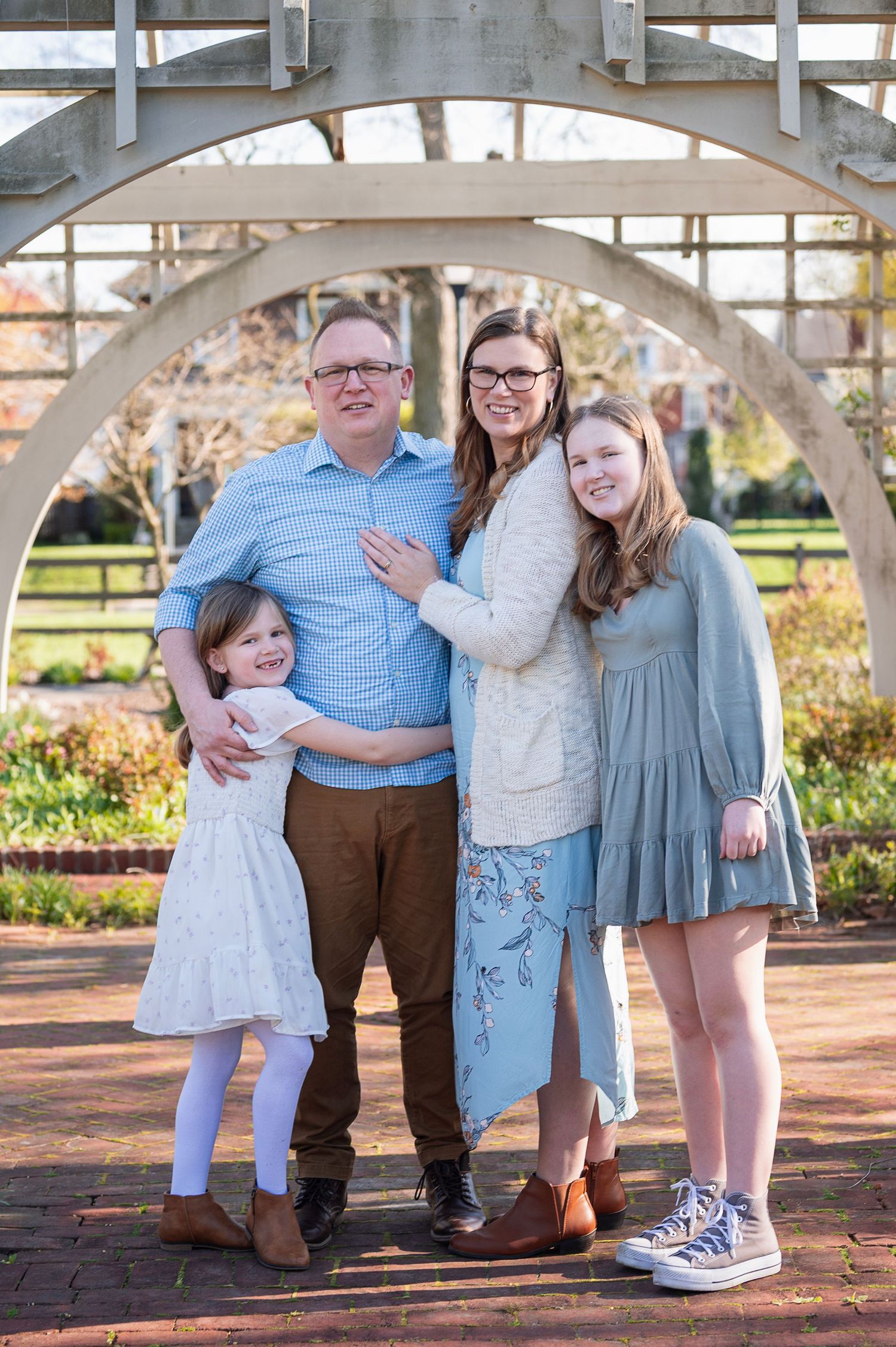Parents with three daughters pose under garden trellis during a springtime Boundless Joy mini session
