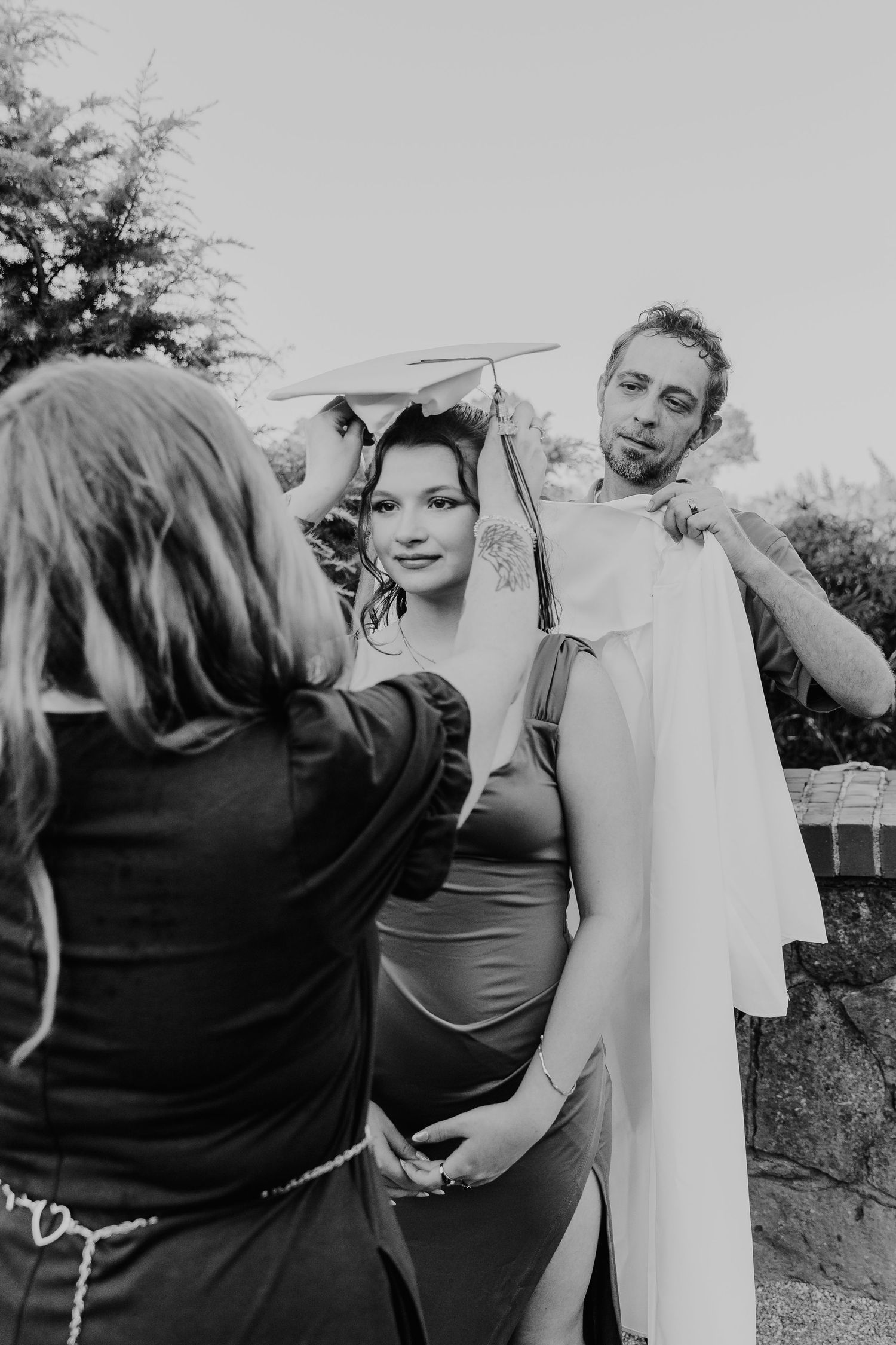 A black and white candid outdoor photo shows a preparation moment during what appears to be a wedding ceremony.