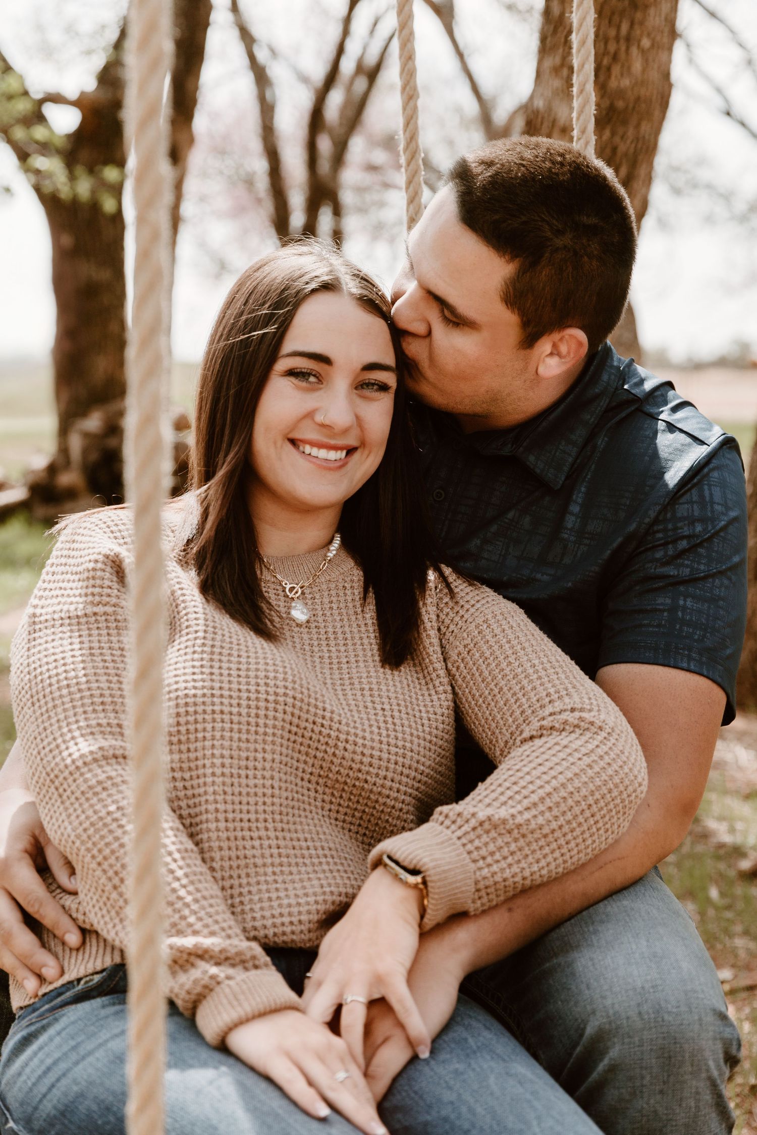 Romantic outdoor couple photoshoot featuring a cream sweater and casual denim clothing in a natural wooded setting.