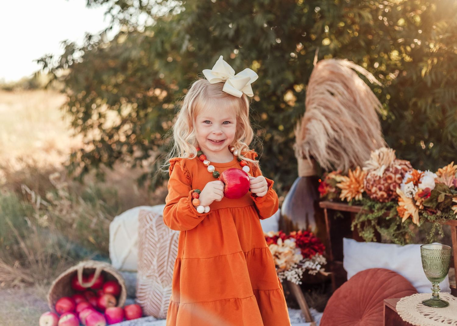 Smiling child in orange dress outdoors at autumn picnic setting with flowers during golden hour sunset.