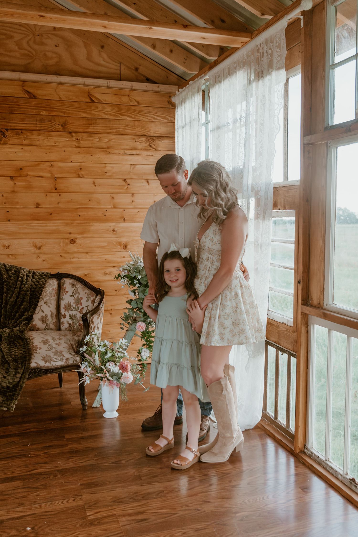 A heartwarming family moment captured inside a rustic wooden cabin with floor-to-ceiling windows and floral decor.