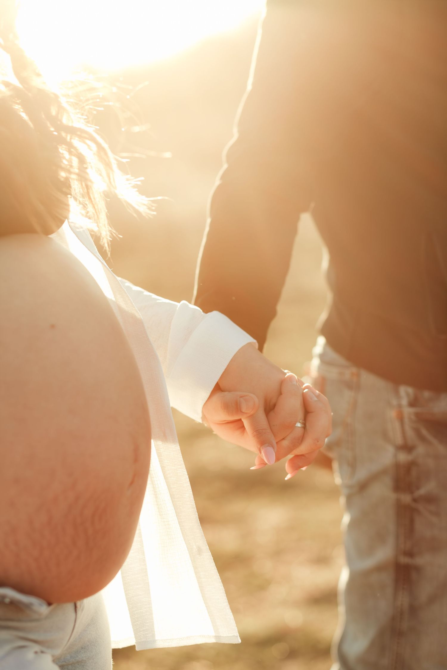 A couple holding hands in warm sunset lighting with a romantic atmosphere in an outdoor setting.