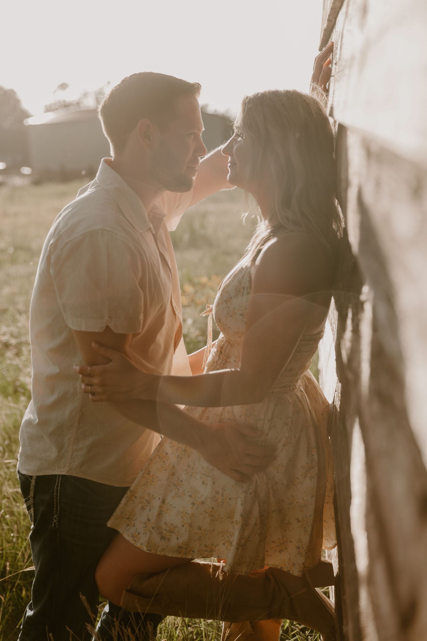 A romantic couple embraces in golden sunlight against a rustic backdrop during a countryside photoshoot.