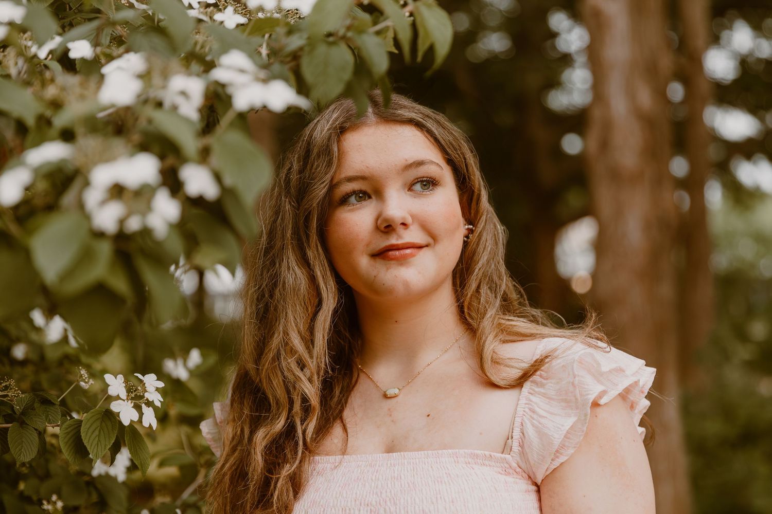 Portrait photograph in a garden setting surrounded by delicate white flowers and greenery.