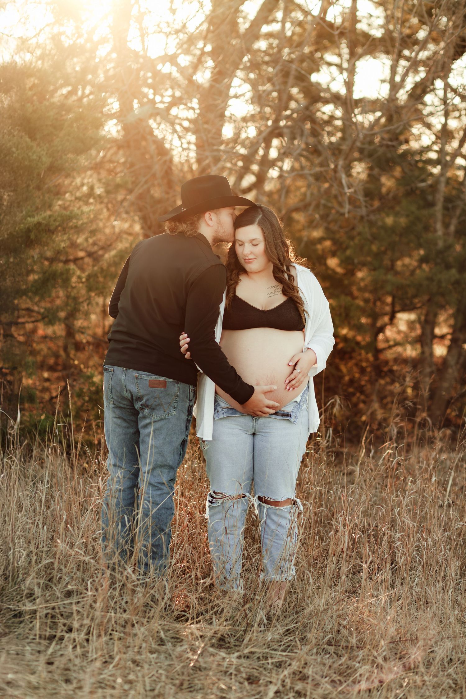 Two people in casual denim embracing in a golden-lit field of tall grass during sunset.