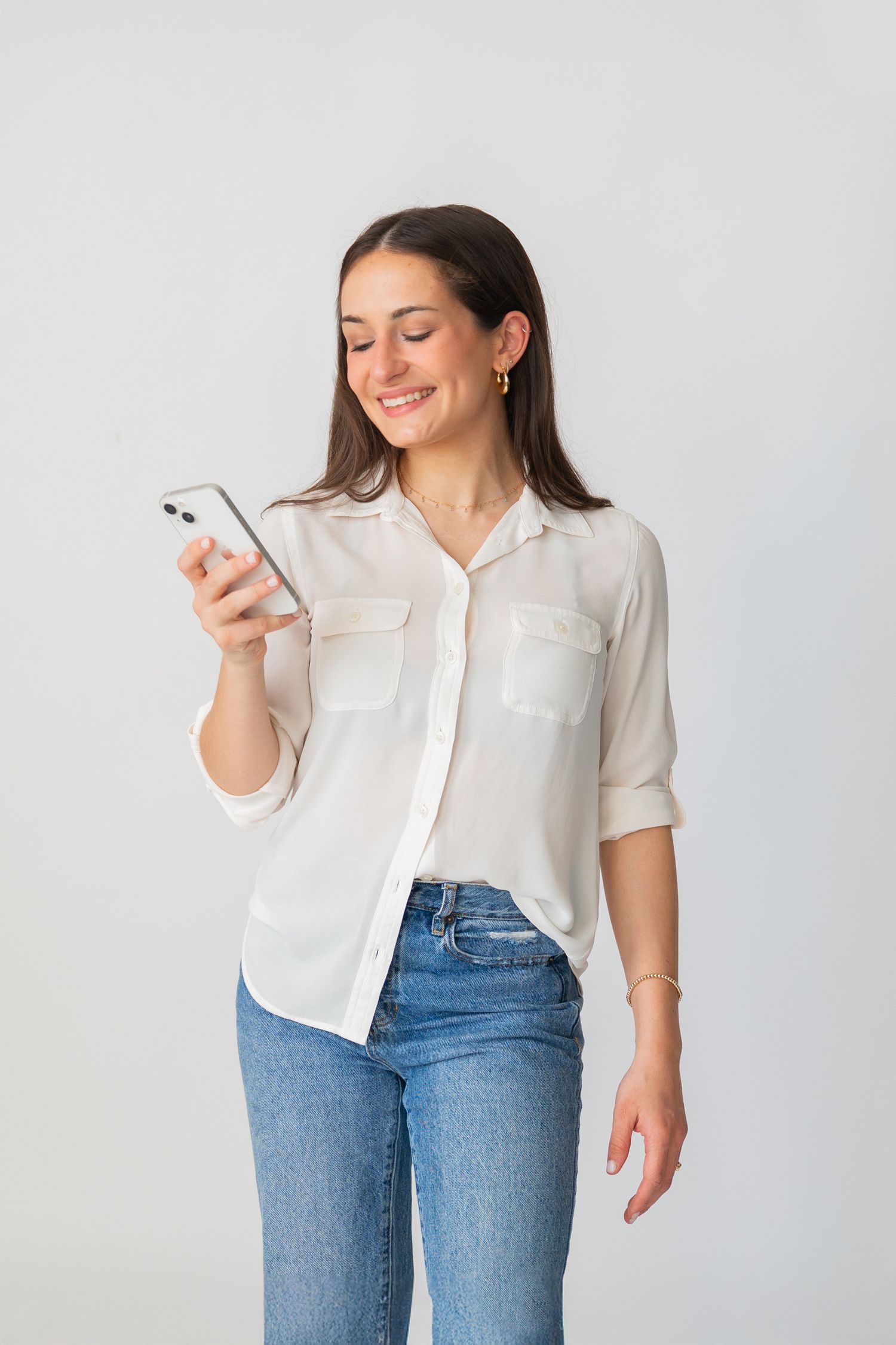 Photographer Kristin Ardese in white shirt and jeans checking phone against plain white backdrop.