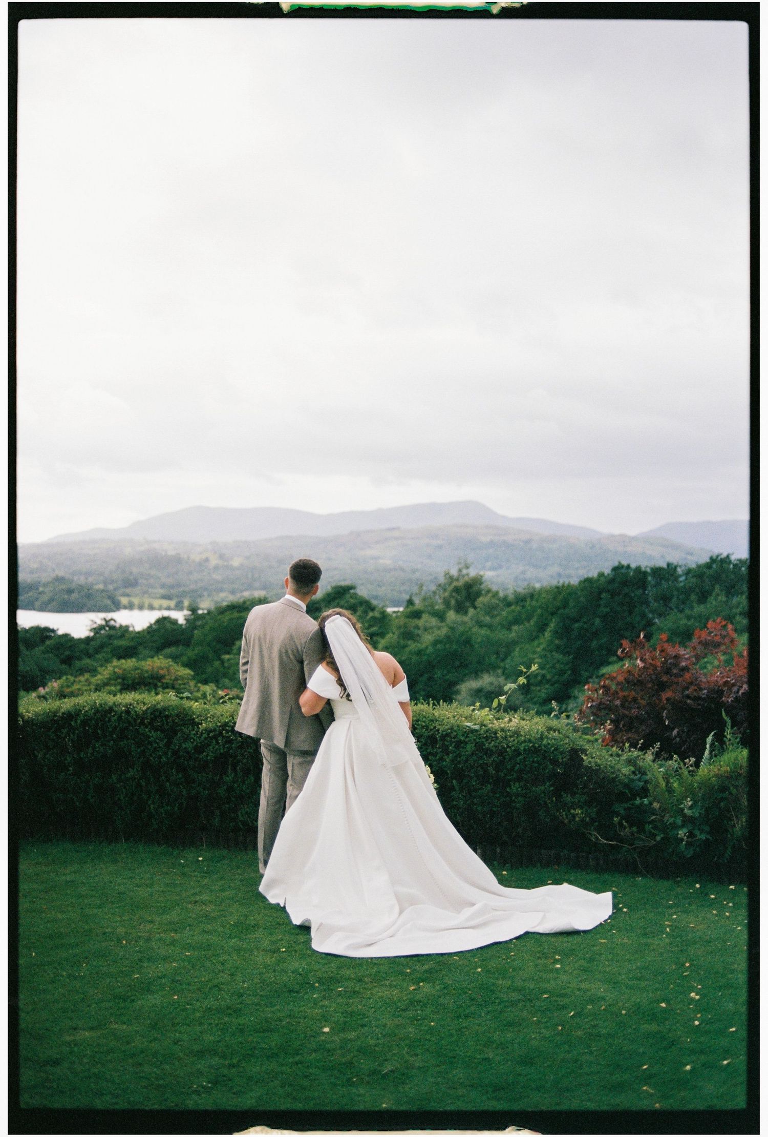 A bride and groom admire the scenic mountain landscape from a lush garden overlook on their wedding day.