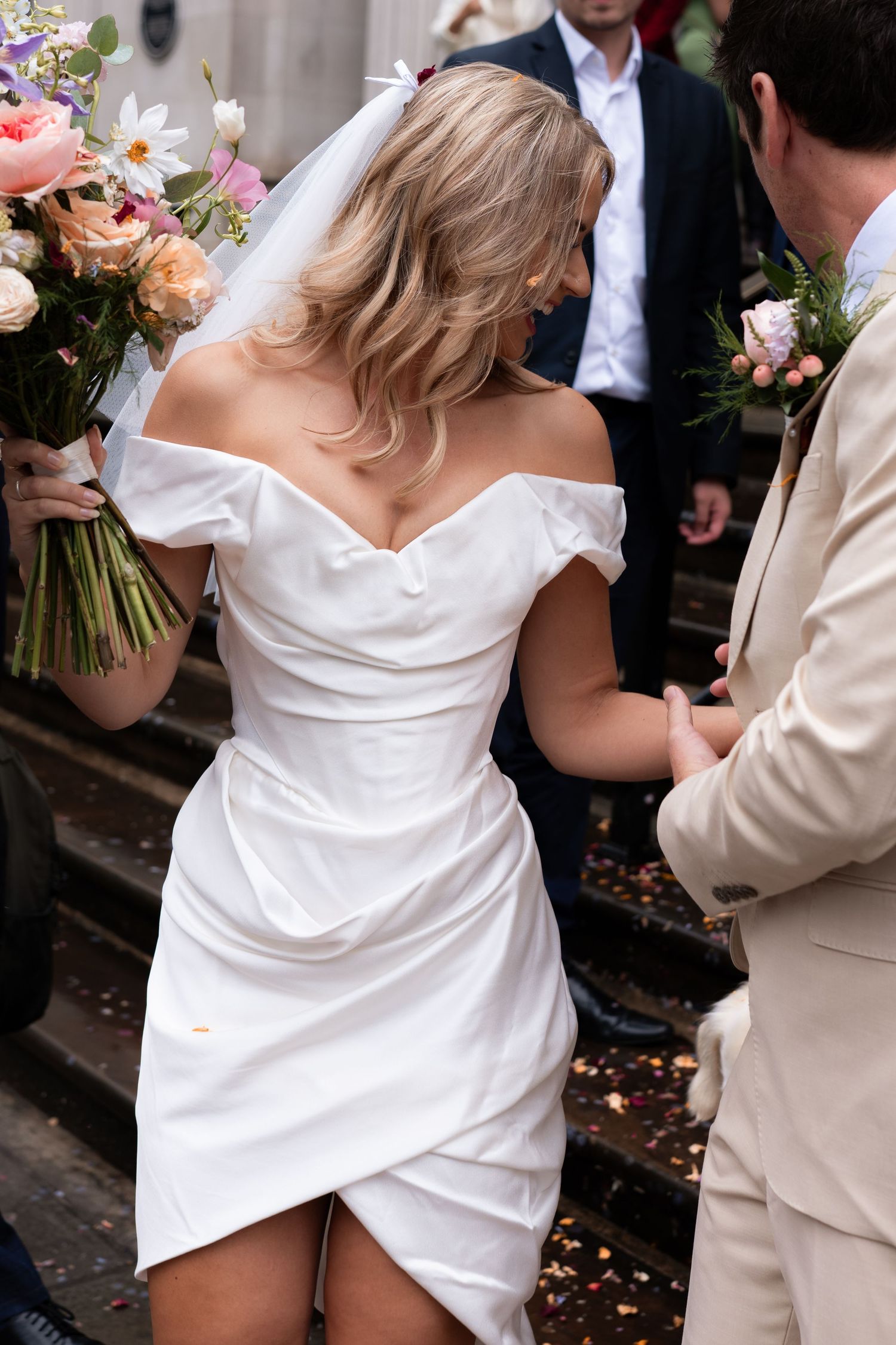 Multiple sequence showing a couple walking down outdoor stairs with the bride wearing a short white wrap dress and holding flowers.
