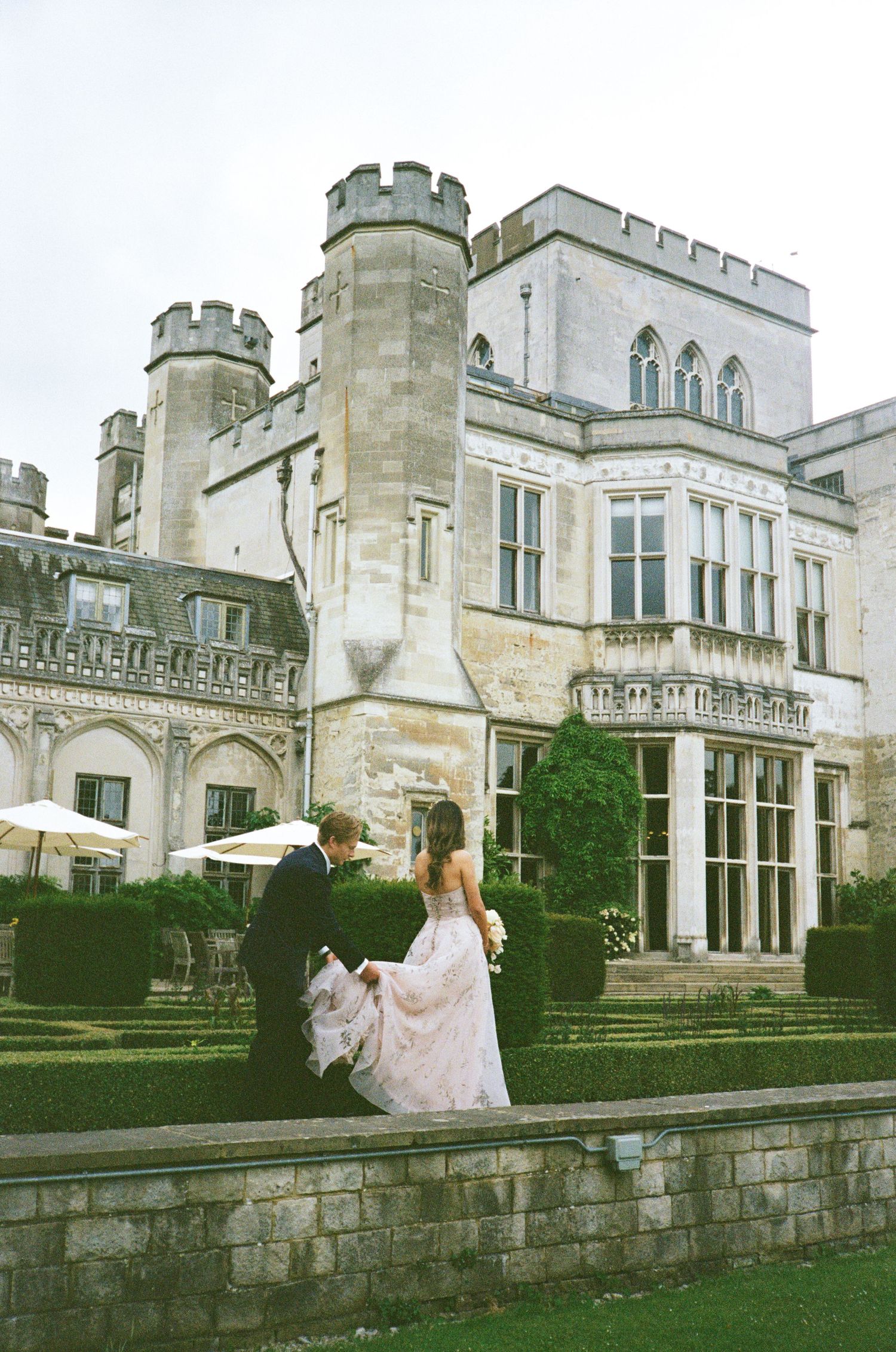 Elegant castle wedding venue with Gothic architecture features stone turrets and a woman in flowing gown on the grounds.