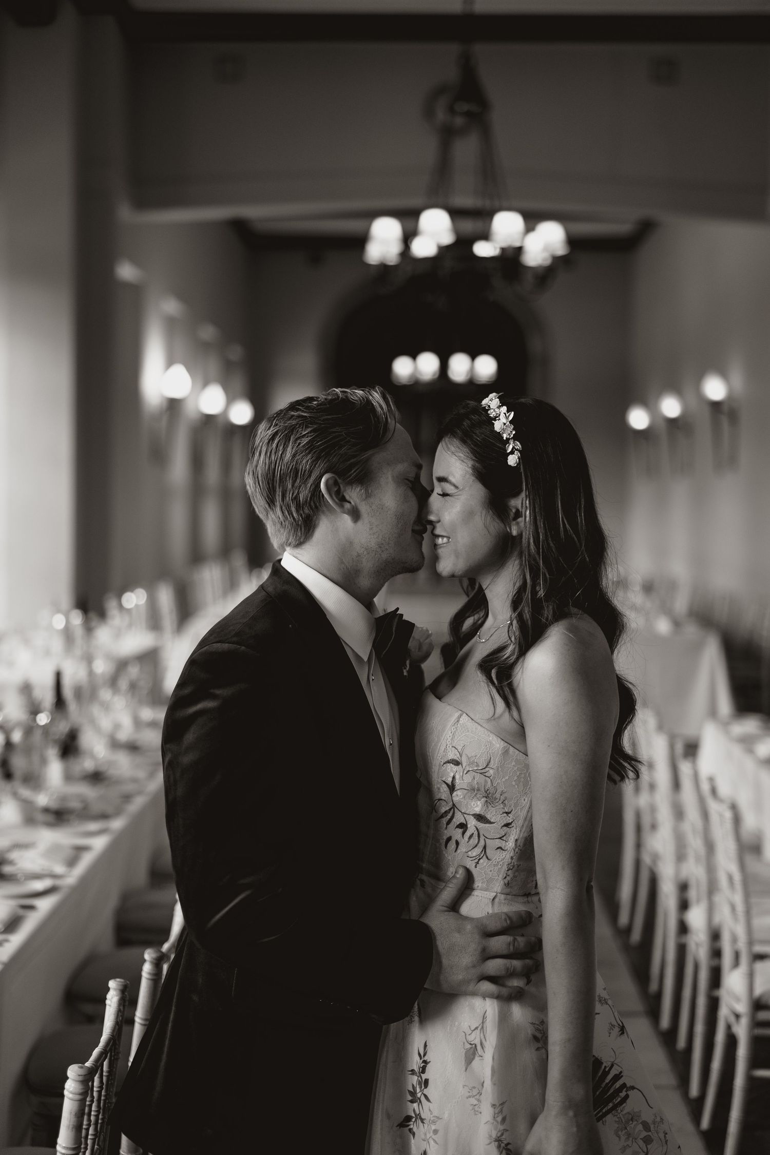 A romantic black and white wedding photo of a couple sharing an intimate moment in an elegantly decorated reception hall.