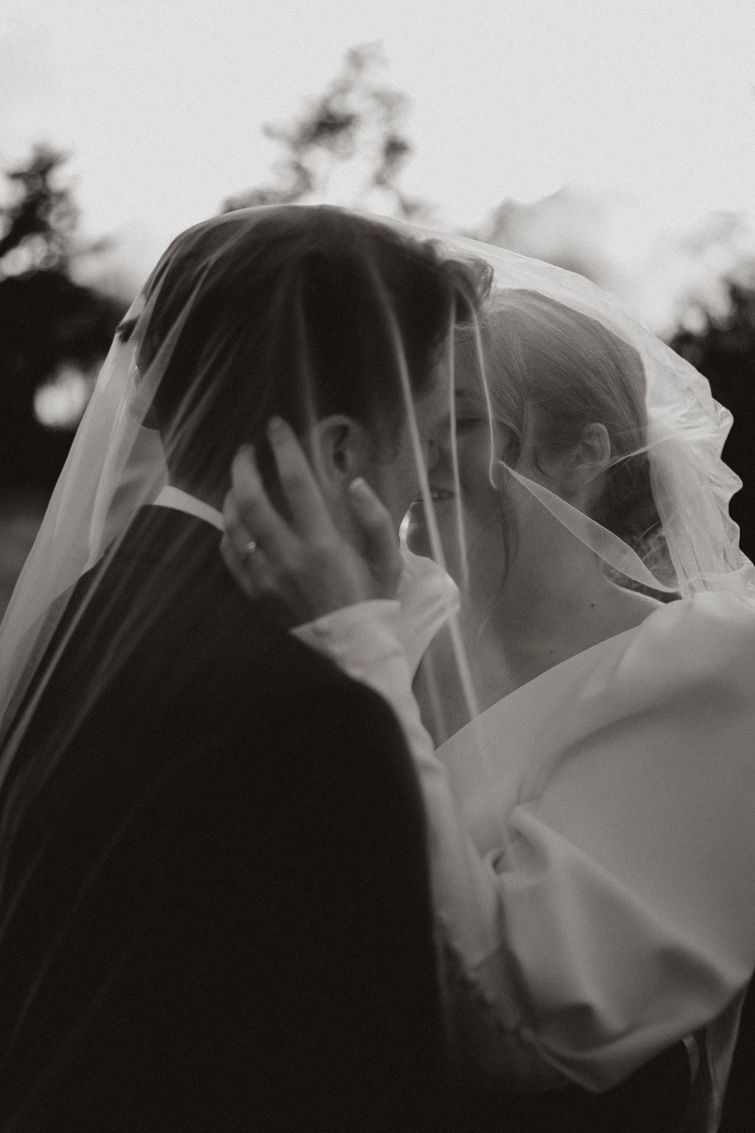 A romantic black and white photo sequence capturing a couple's tender kiss beneath a flowing white wedding veil.
