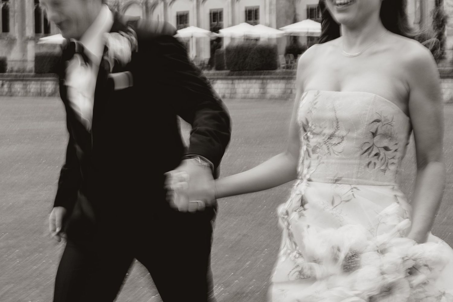 A blurred black and white motion photograph of a couple in wedding attire walking together outside.