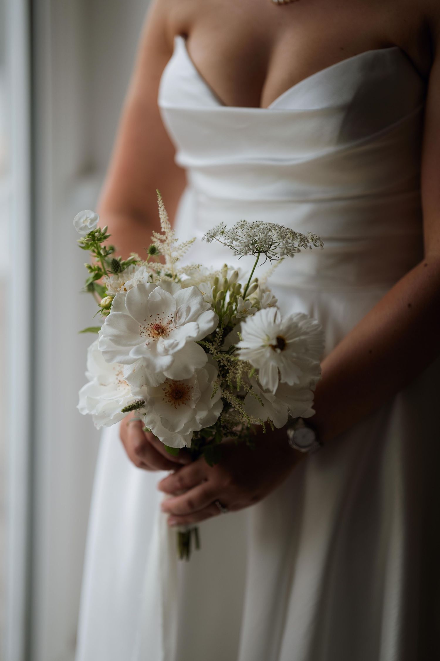 Elegant white wedding bouquet with delicate blooms held against a white dress with a classic neckline.