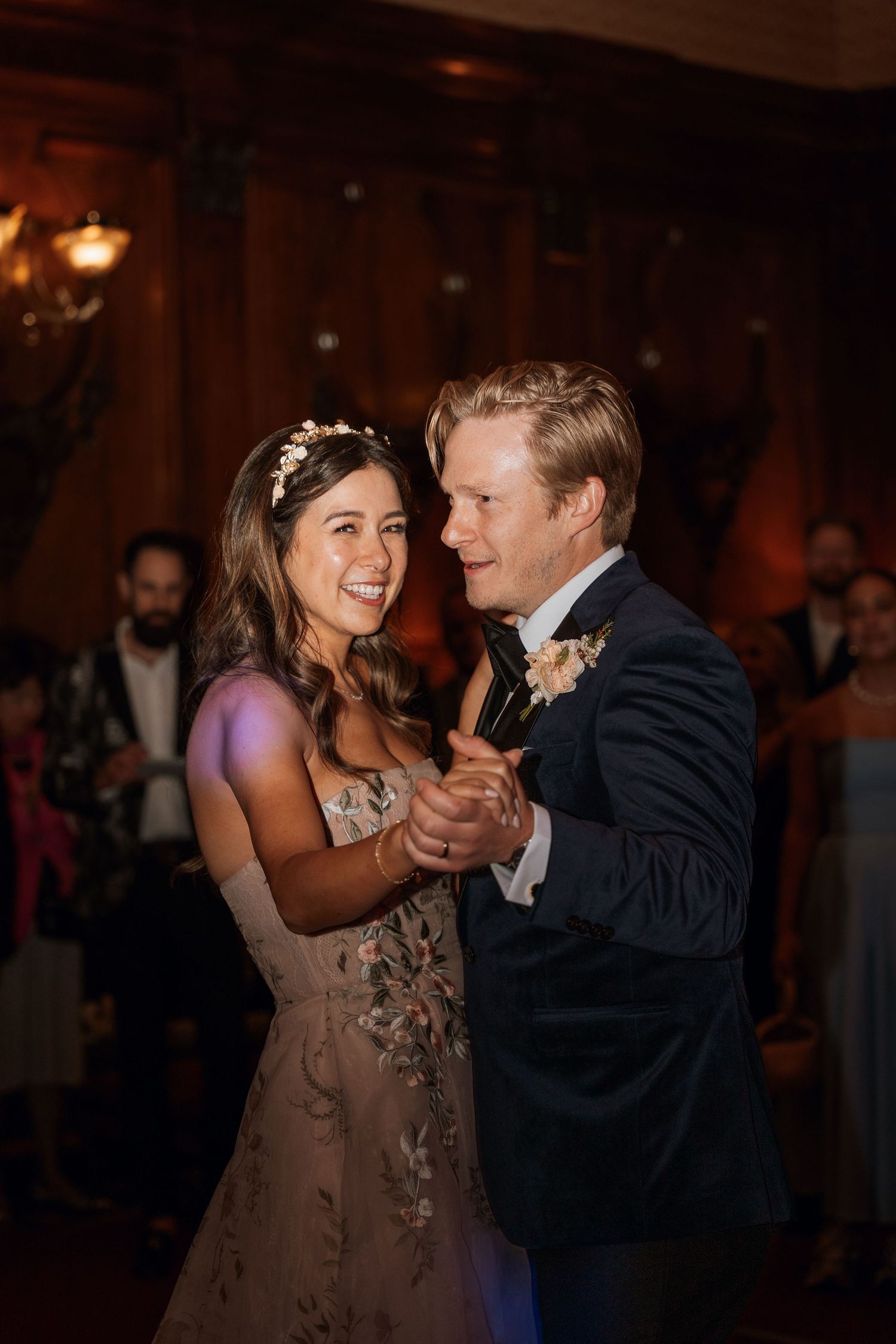 A couple shares a joyful dance moment at their wedding reception in a warmly lit ballroom.