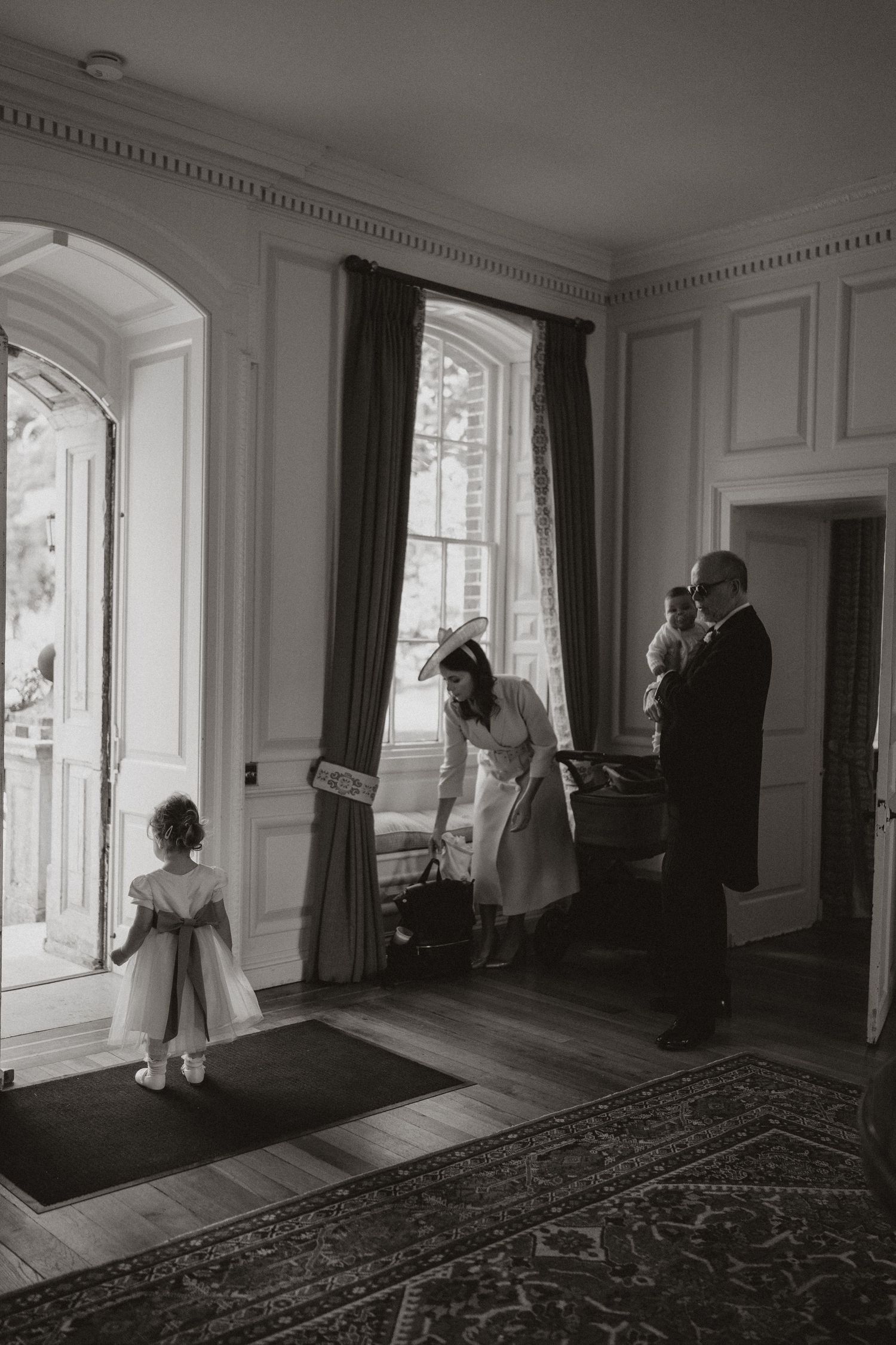 A black and white photograph shows people in an elegant room with tall windows, crown molding and dark curtains.