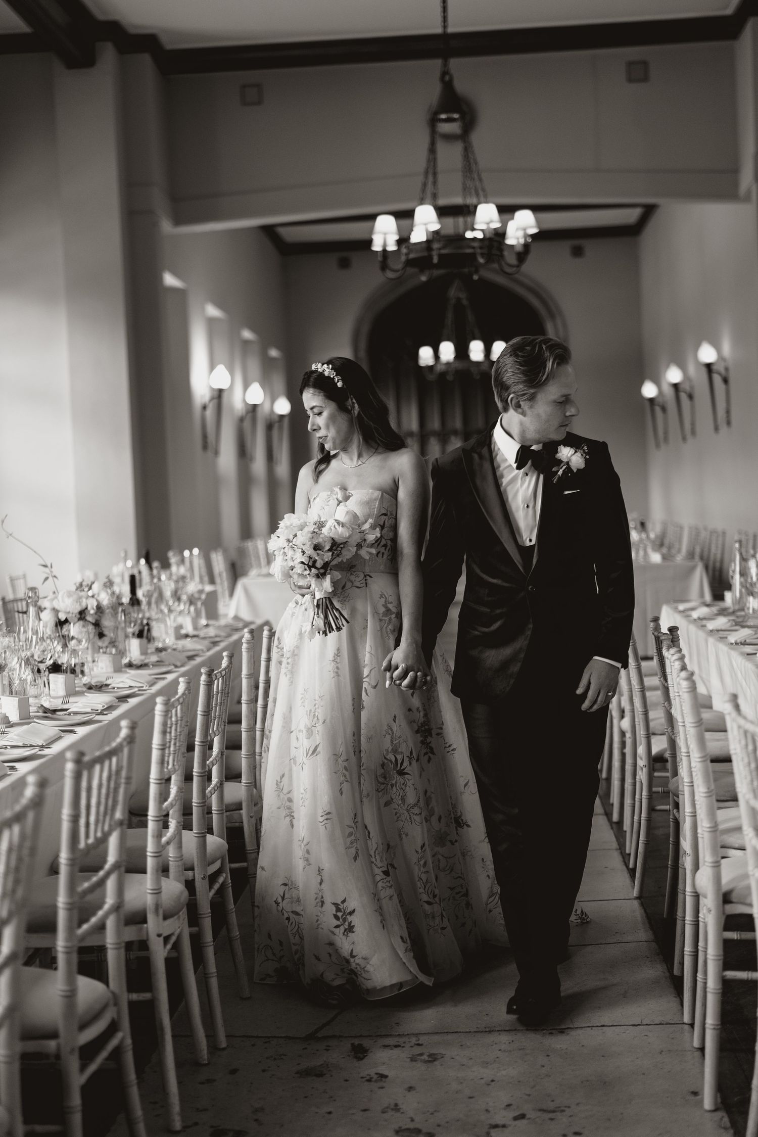 Black and white wedding photo showing a room with elegant table settings and chairs arranged for a formal reception.
