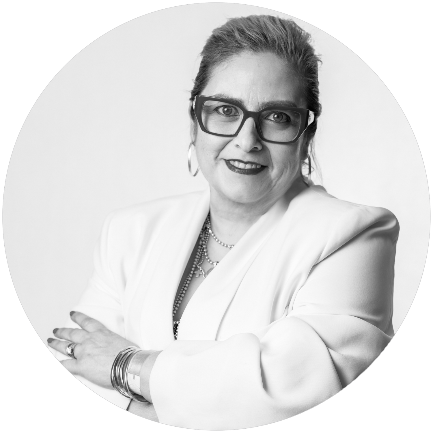 Professional headshot of a smiling business person wearing glasses, a white blazer and silver jewelry against a light background.