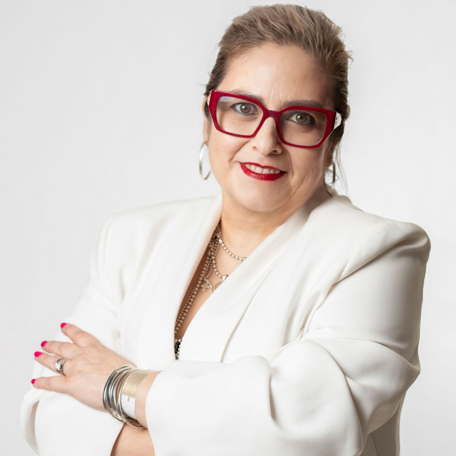 Professional woman in white blazer and red glasses with silver jewelry smiling against light background.