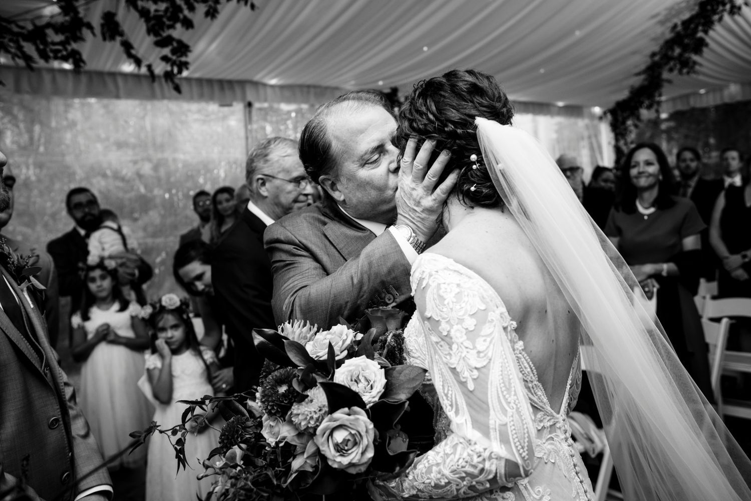 A tender moment between newlyweds during their first kiss at their wedding ceremony surrounded by guests and decor.