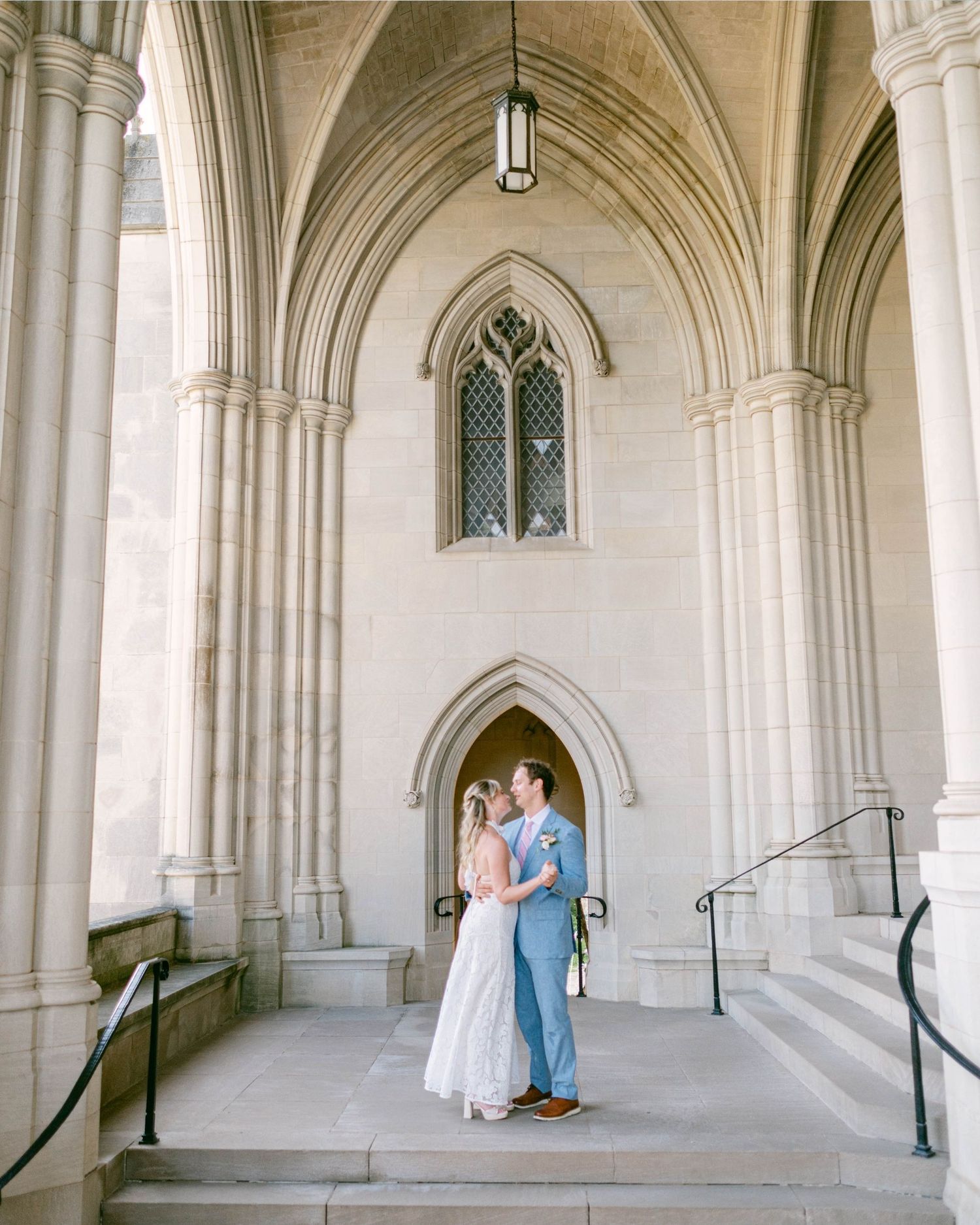 A couple embraces through an elegant Gothic-style stone archway corridor with white vaulted ceilings at the National Cathedral in DC.
