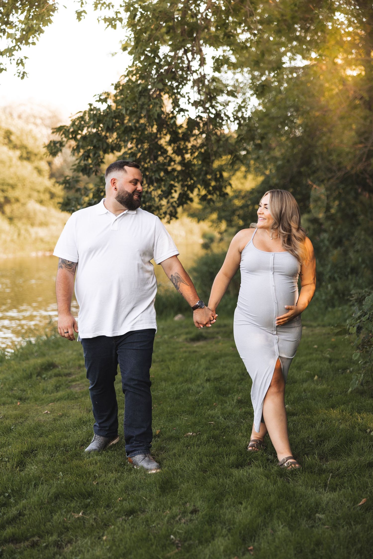 Couple in casual attire enjoying playful moments on a grassy hillside during sunset.