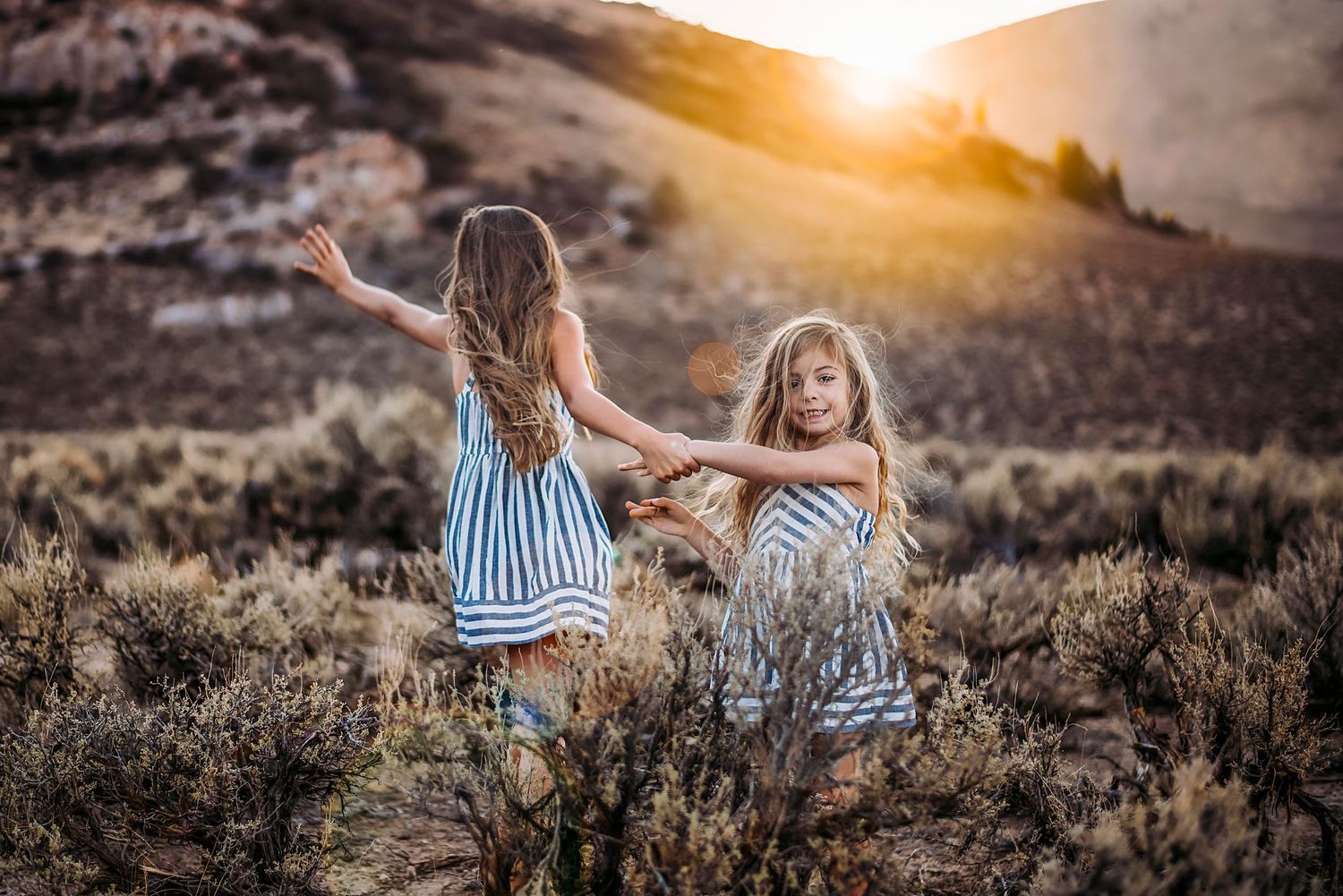two young girls dance in the sagebrush on a warm sunny evening during a family photography session in Ellensburg, WA