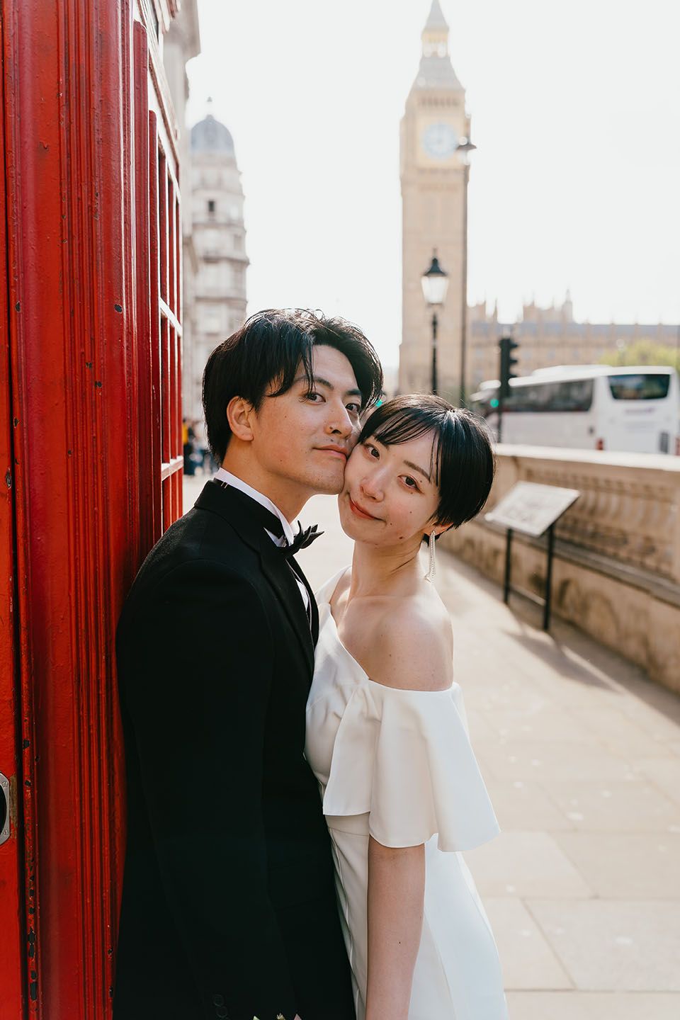 A couple poses together near a red phone booth with London's Big Ben visible in the background.