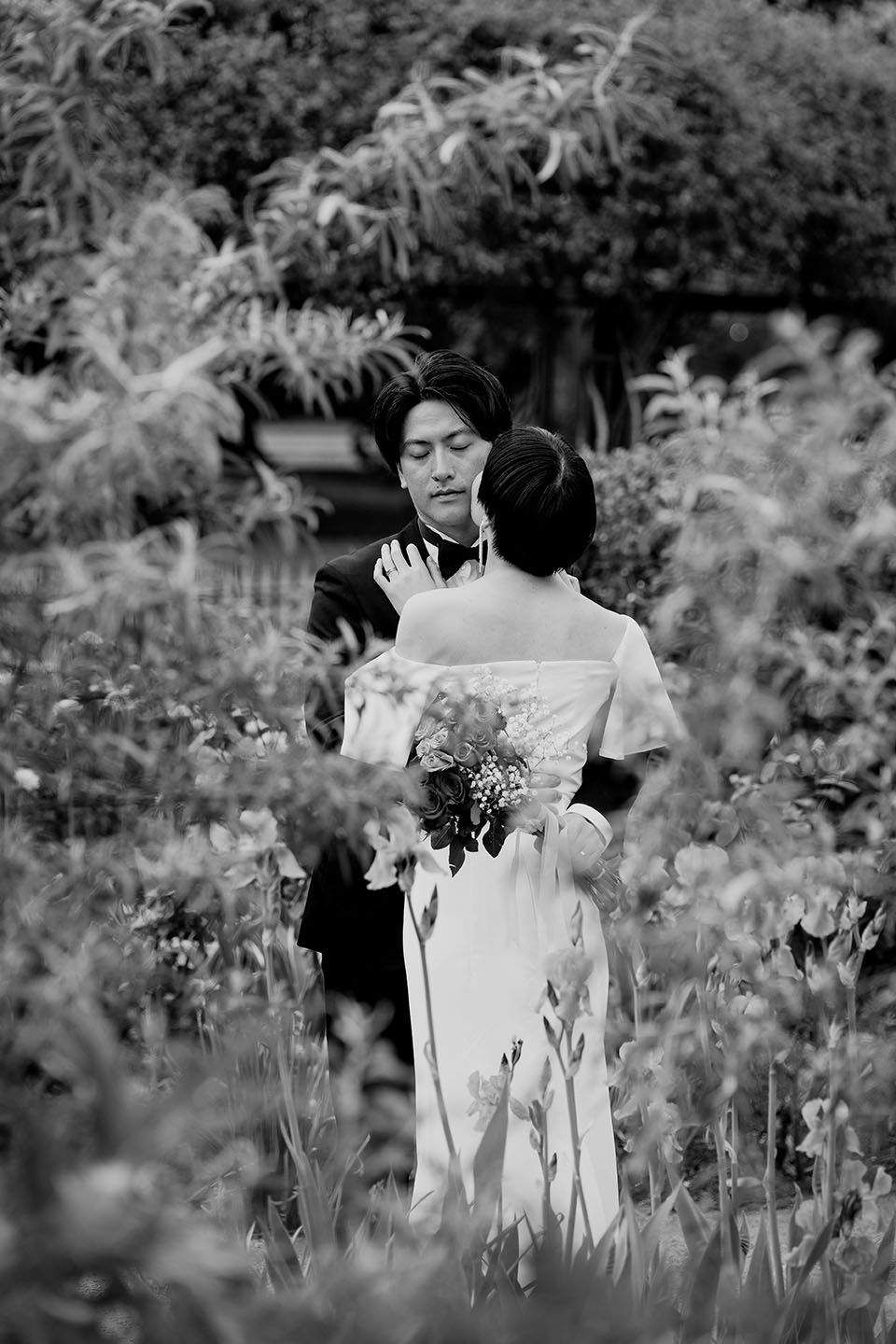 Black and white wedding photo showing couple in outdoor garden with flowers, bride holding bouquet.