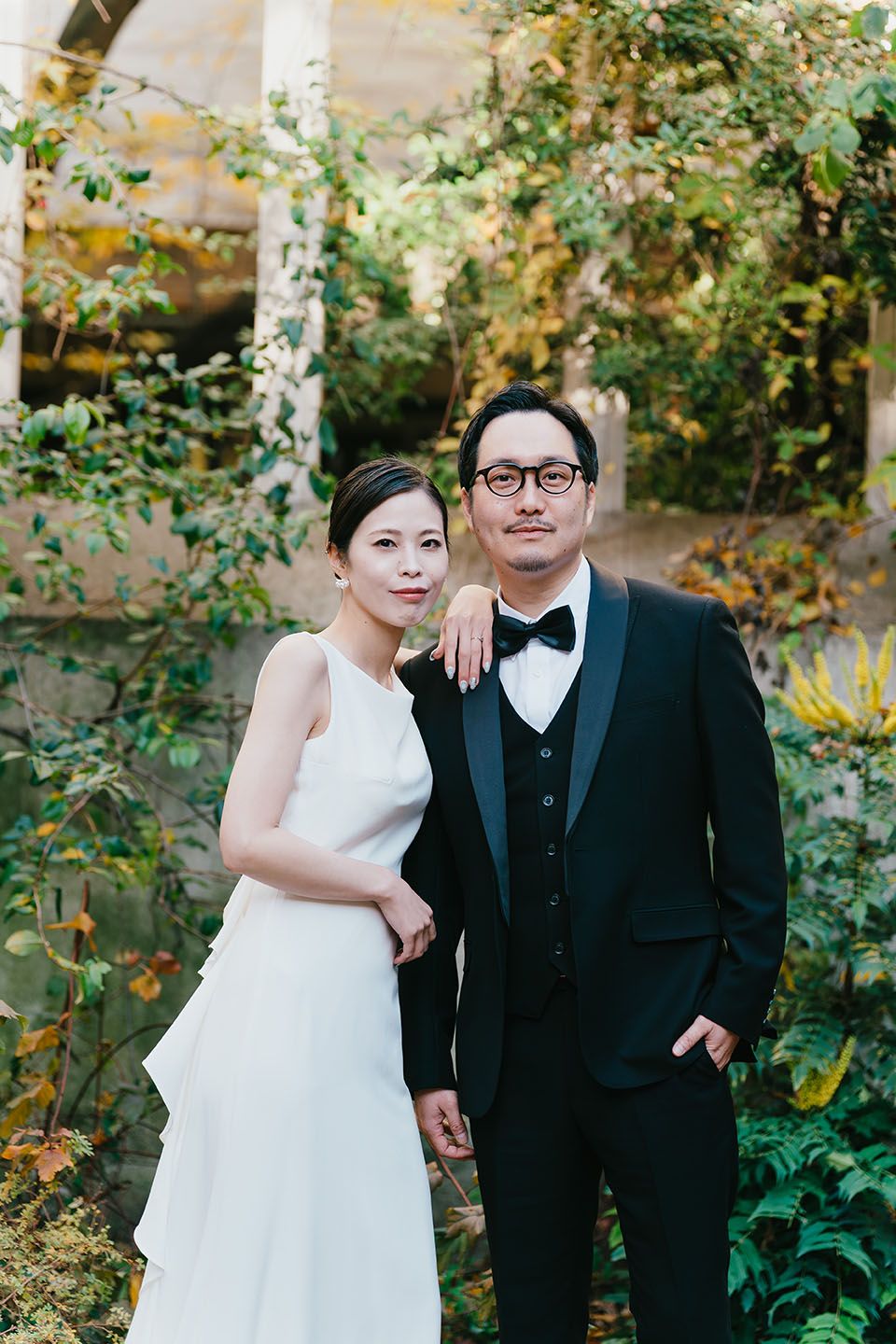 Wedding couple poses together in garden setting with lush greenery and natural lighting.