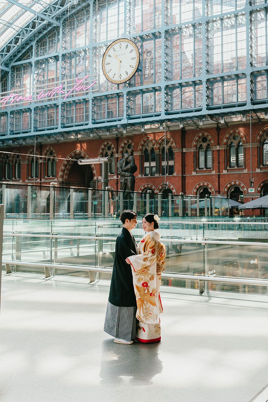 Two individuals sit together in an elegant glass-roofed interior space at St. Pancras Station in London.