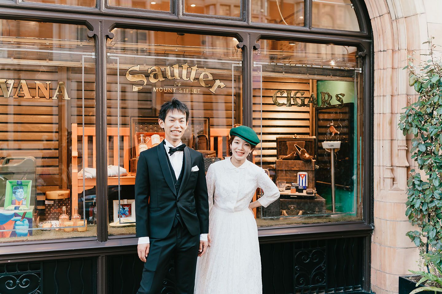 Wedding couple poses in front of a vintage storefront with arched window and rustic decor.