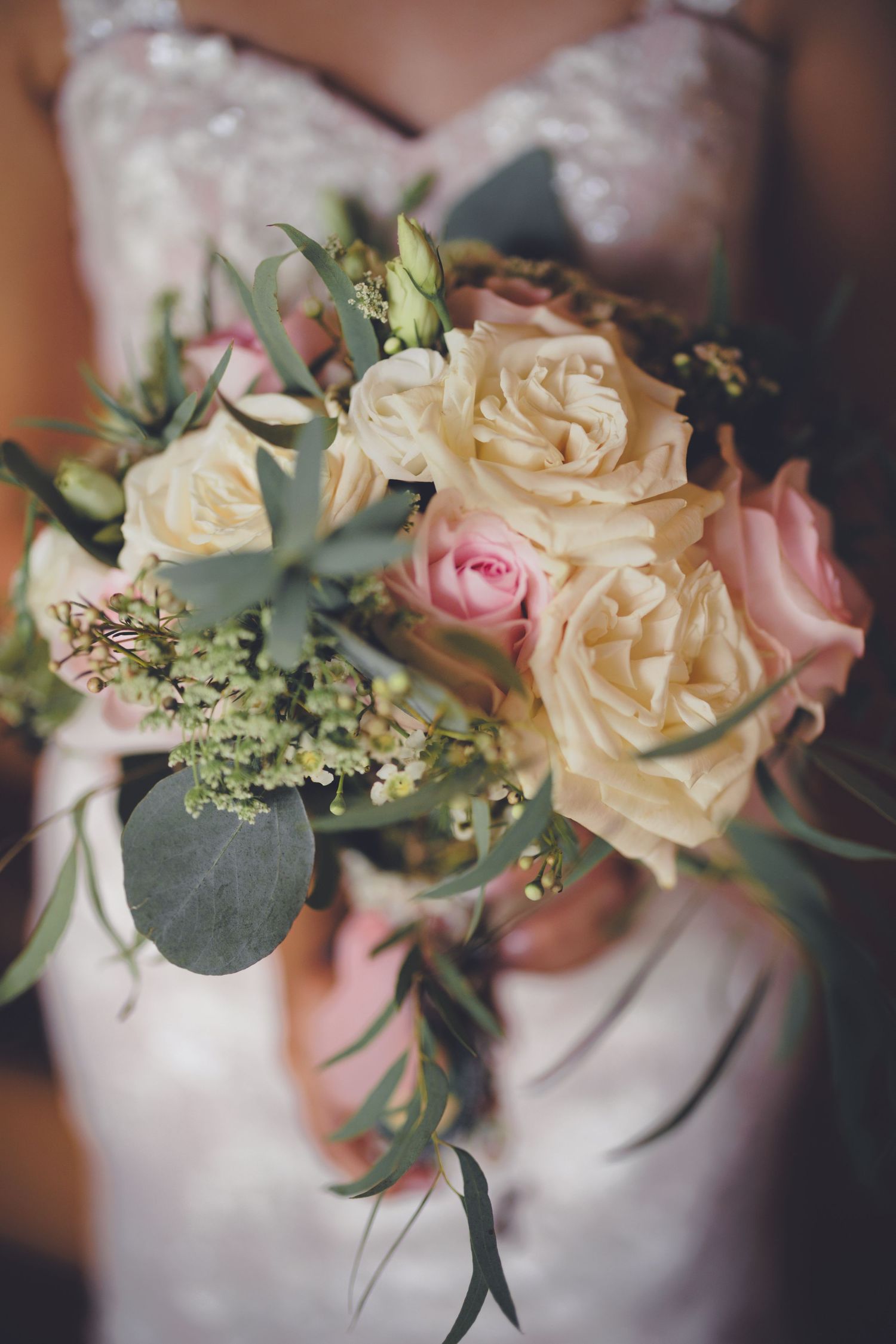 A close-up of a bridal bouquet featuring soft pink and cream roses, with greenery and delicate accents.