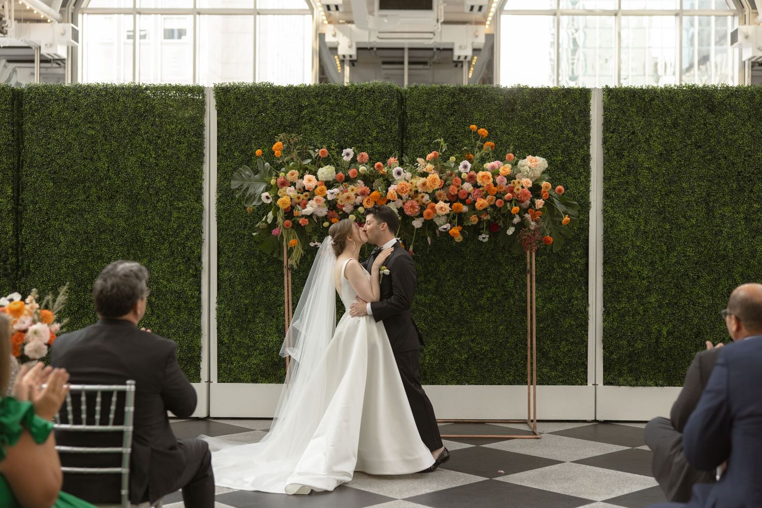 Wedding ceremony at a modern greenhouse venue with black and white checkerboard floor.