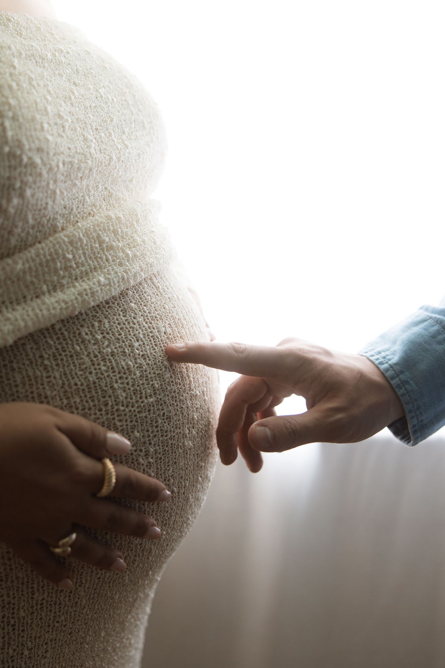 Close-up view of pregnant belly in soft sweater being touched by two hands in gentle, intimate moment.