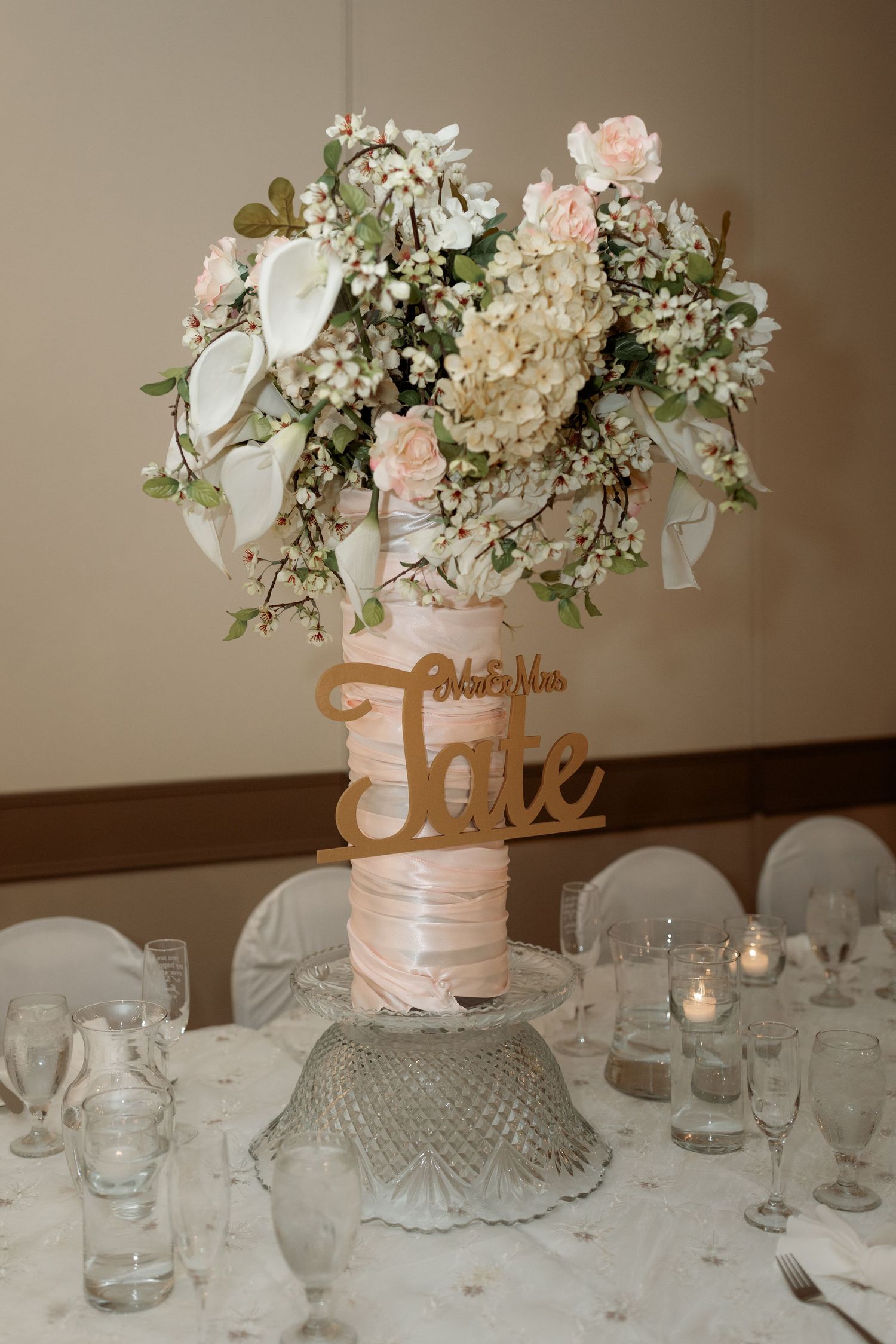 Romantic wedding centerpiece with blush roses and hydrangeas atop a glass stand with illuminated table decor.