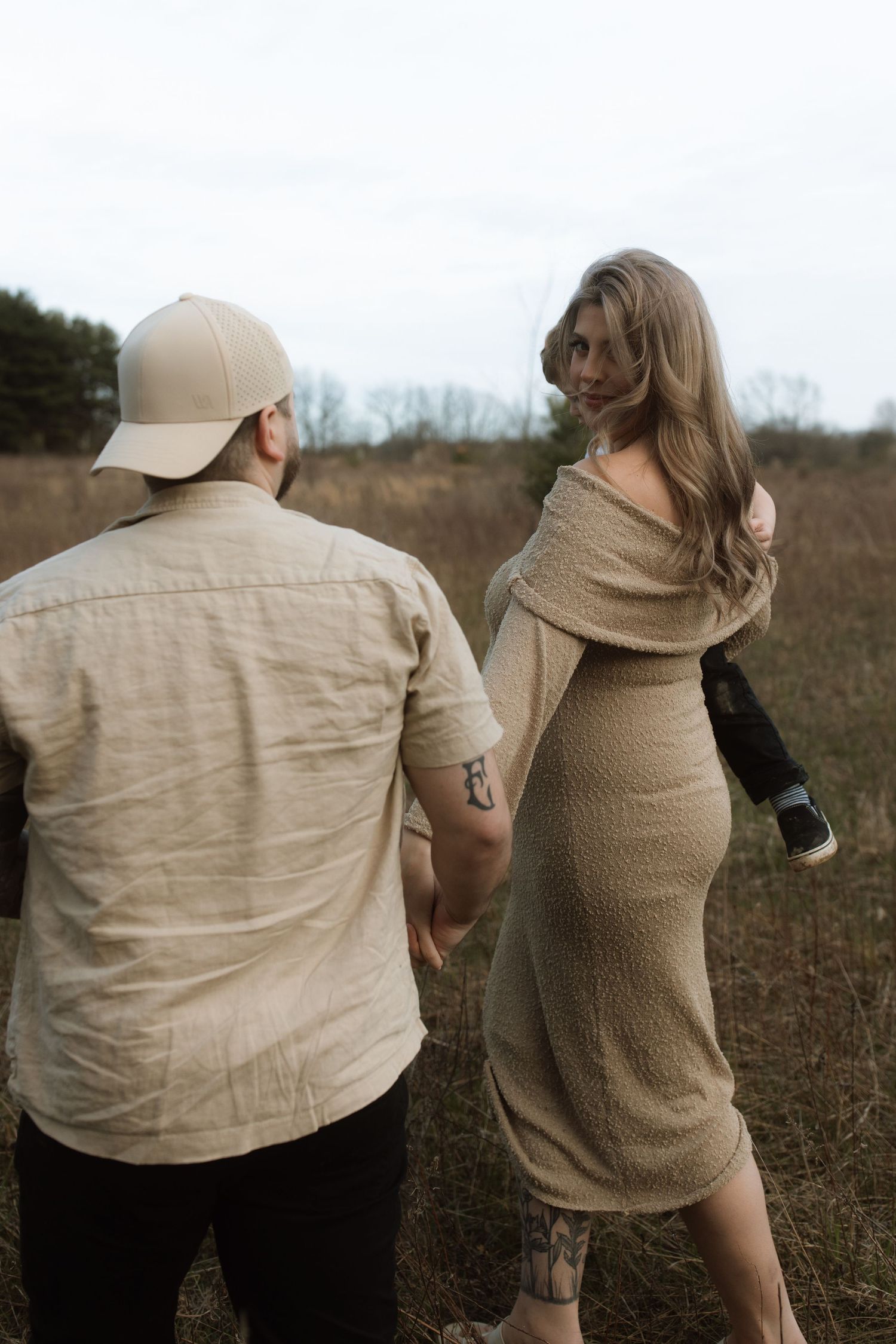 Couple walking together in field wearing neutral tones with child.