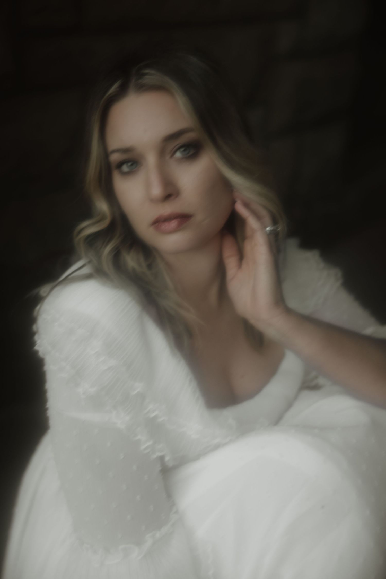 Dreamy portrait of someone wearing a soft white feathered dress in moody lighting with delicate styling.