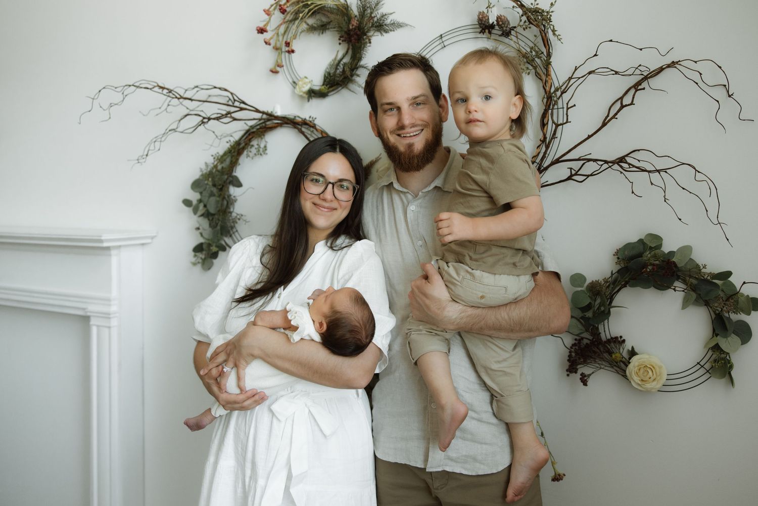 Family with a newborn baby posing in front of a white mantle decorated with natural branches and greenery.