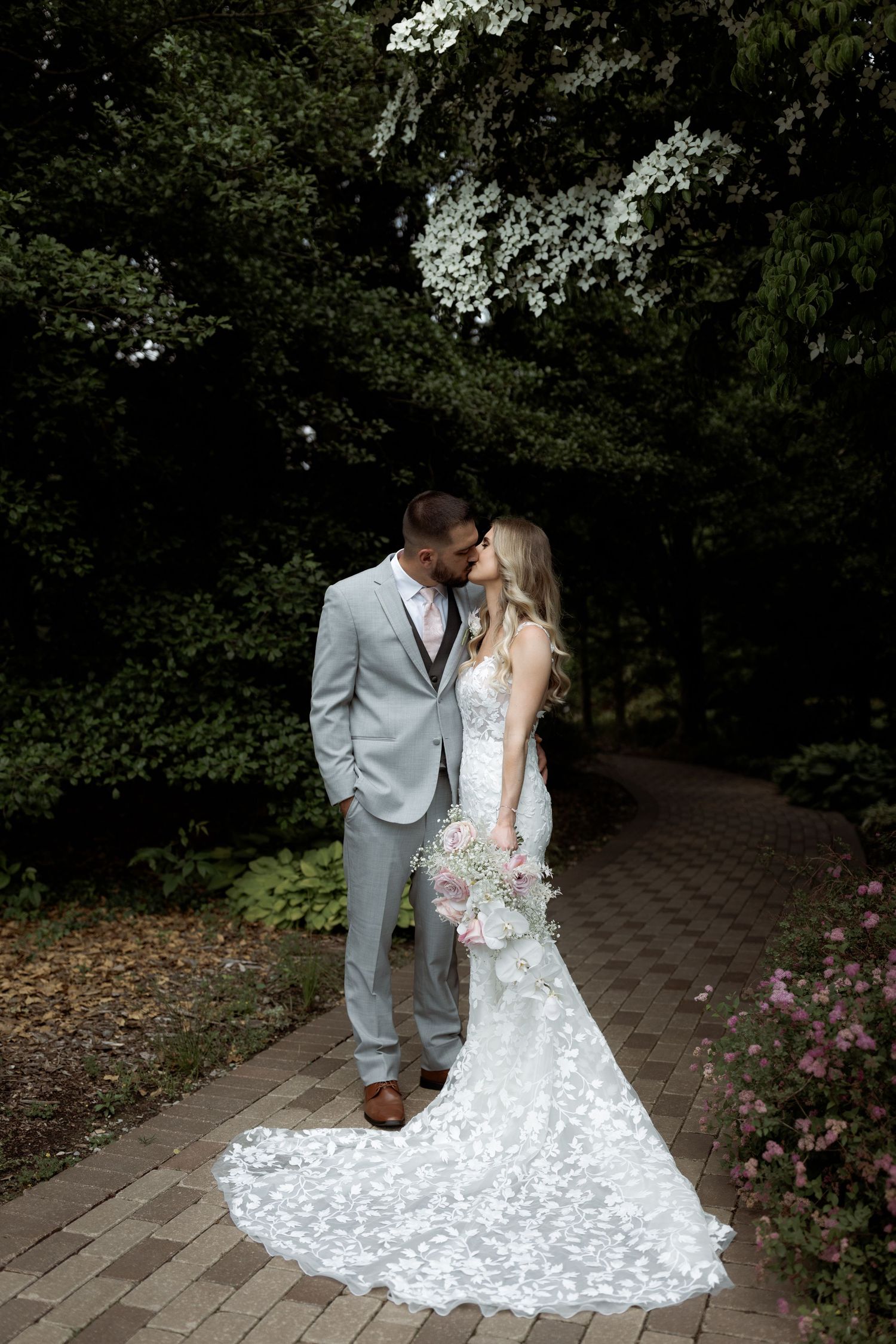 Romantic wedding couple shares tender moments in a garden setting with white lace dress and light gray suit.